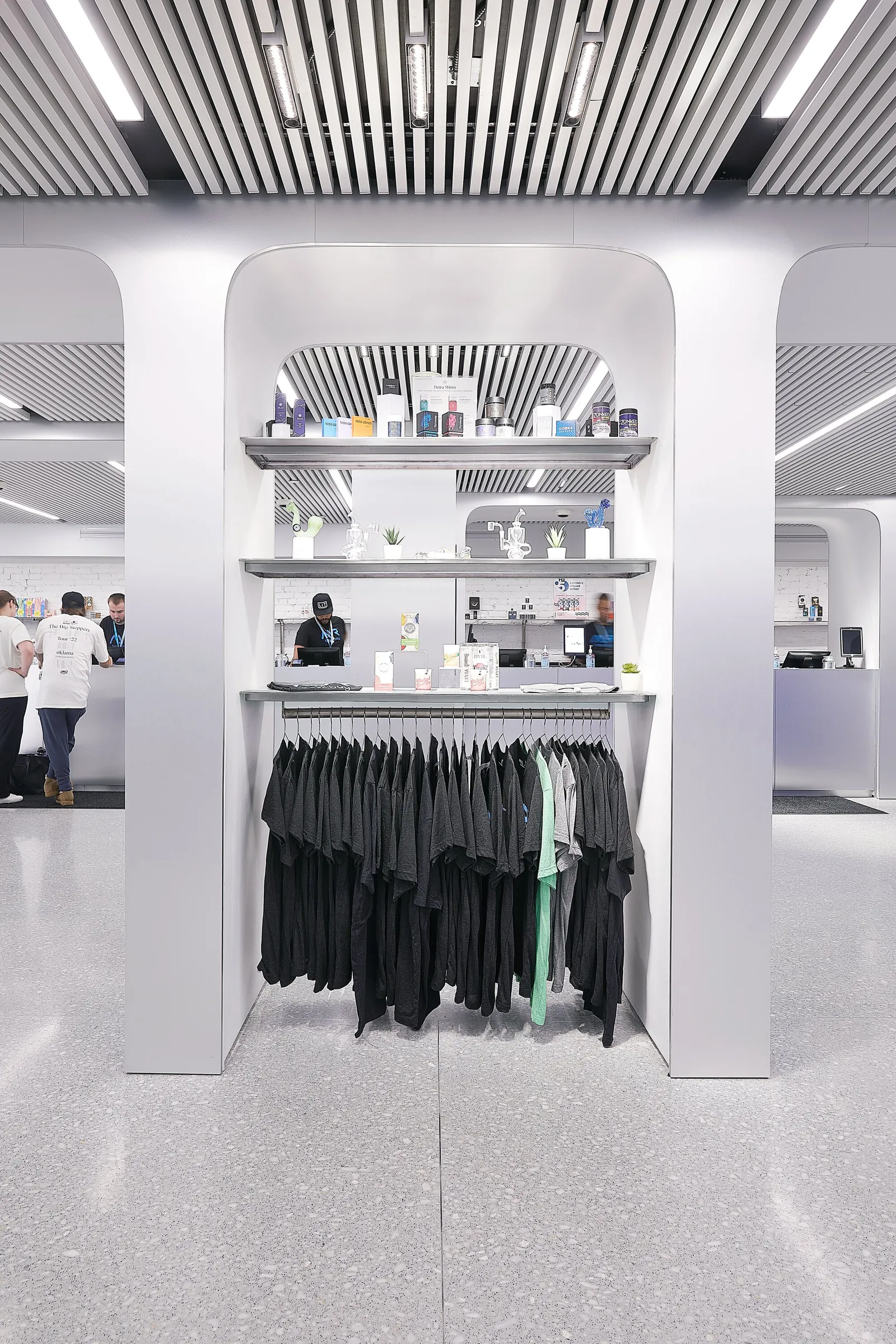vertical view through a white arched portal at a clothing rack and shelves, with a slatted ceiling and staff behind