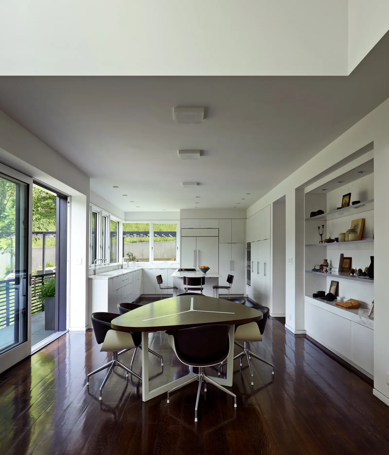 open dining and kitchen room with a triangular dark table, white cabinetry, built-in shelves and dark wood floors