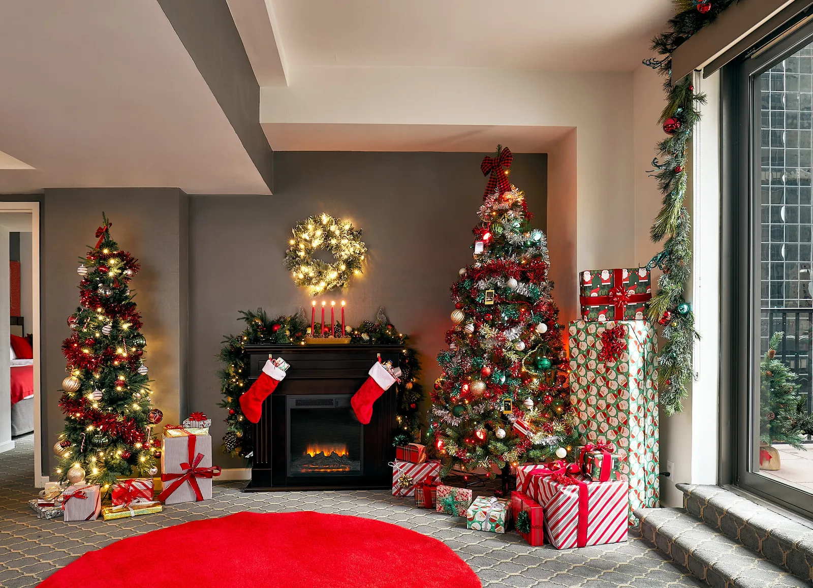 hotel suite living area dressed for christmas with two trees, a fireplace with stockings and a red round rug