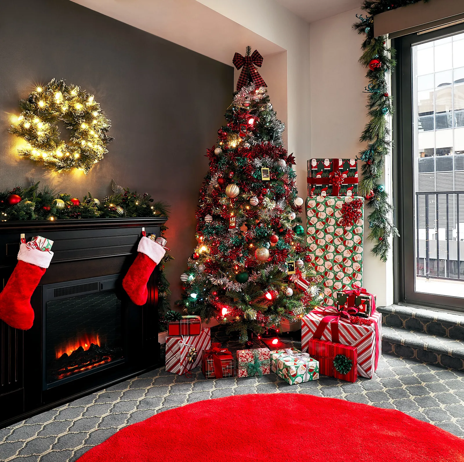 corner of the suite with a lit wreath over a mantel, a tall tree and wrapped gifts beside a balcony window