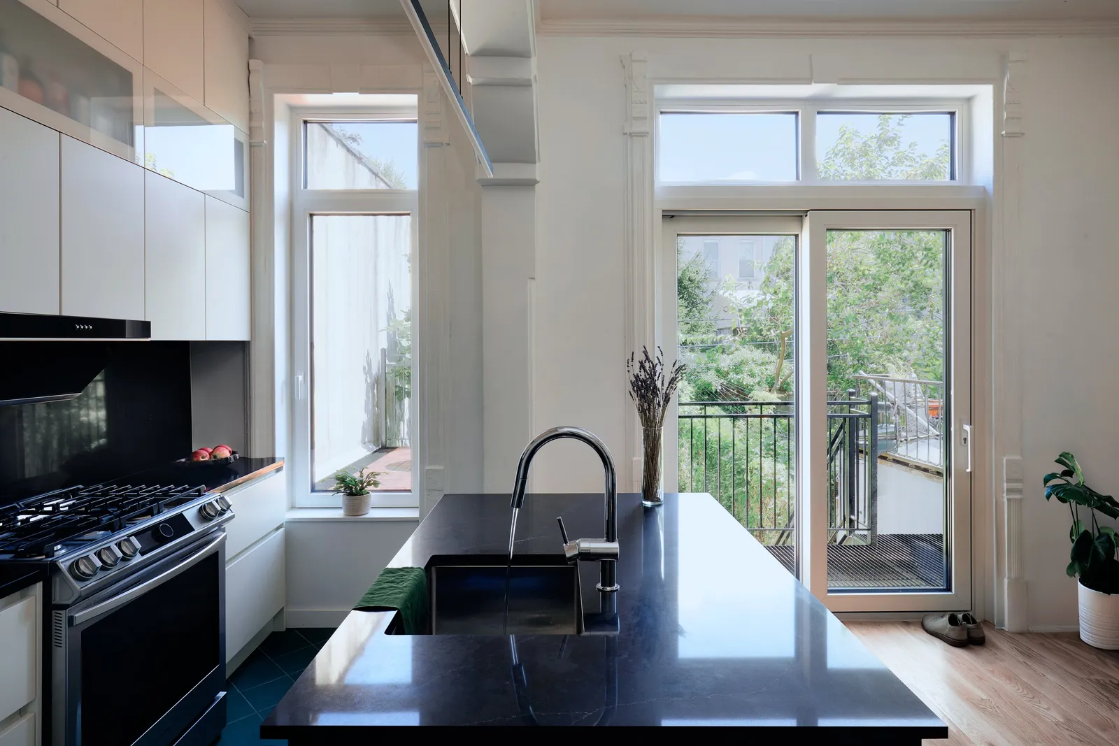 kitchen island with a dark counter and faucet facing a glass door to a balcony, white cabinets and a gas range at left