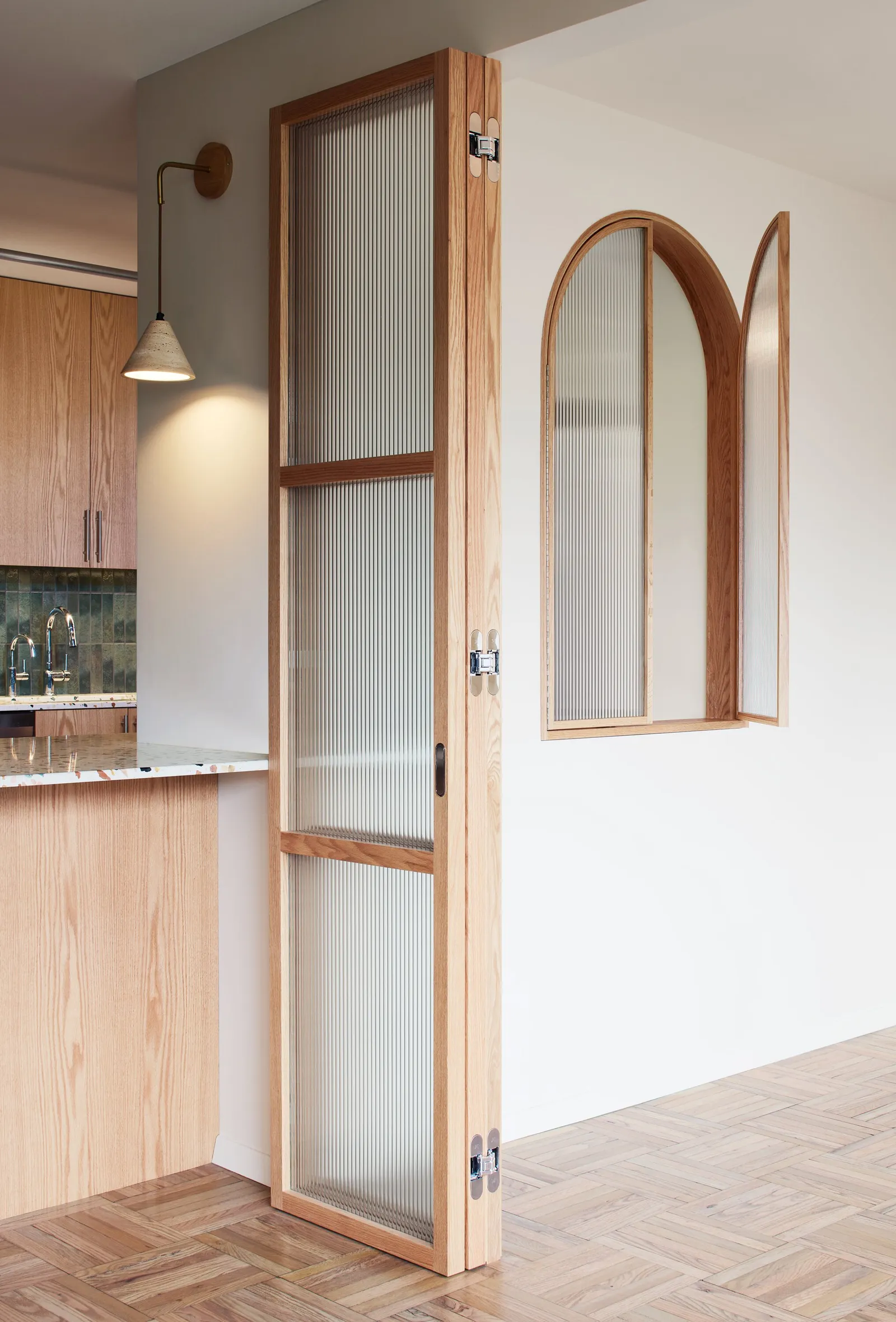 tall folding glass door beside an arched interior window, with kitchen cabinets and a wall sconce