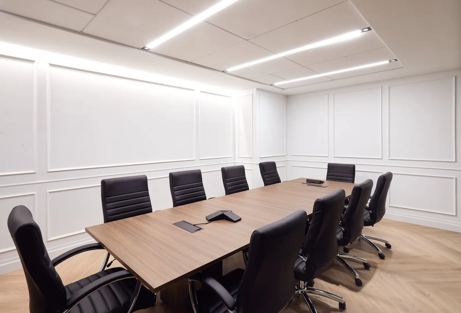 conference room with white wall paneling, light wood table, black leather chairs and strip lights