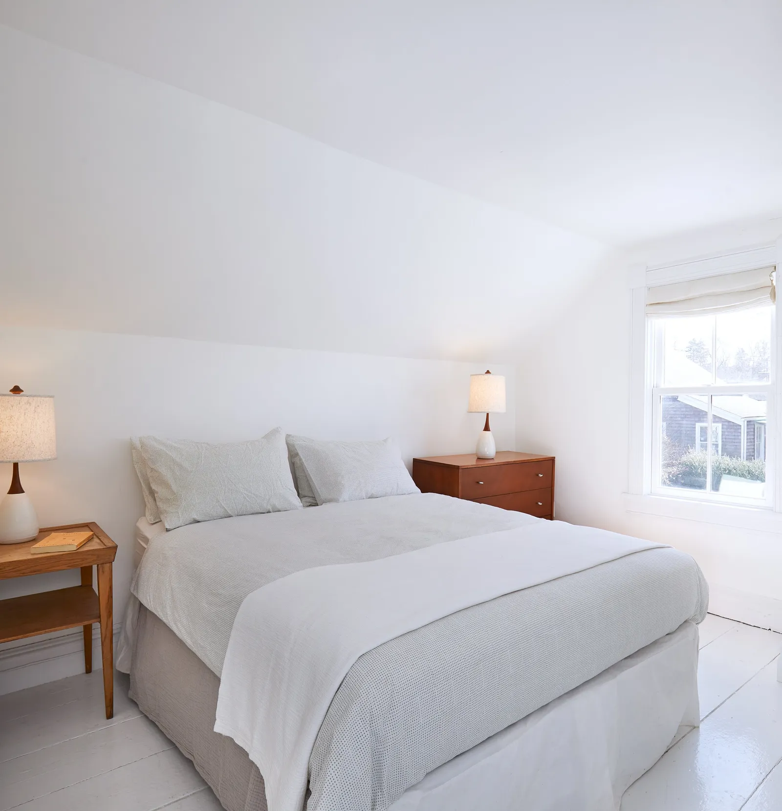 white bedroom with a slanted ceiling, a bed with gray linens, wooden nightstands and lamps