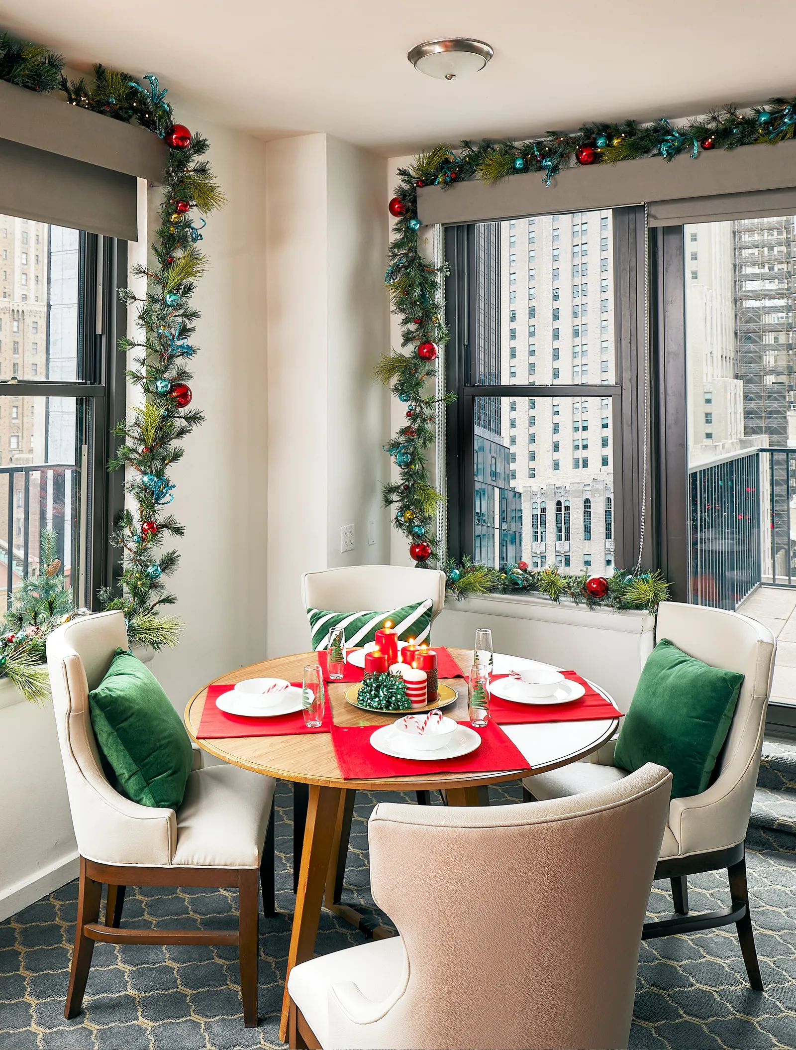 dining nook with a round wooden table set in red and green, garland framing tall city-view windows