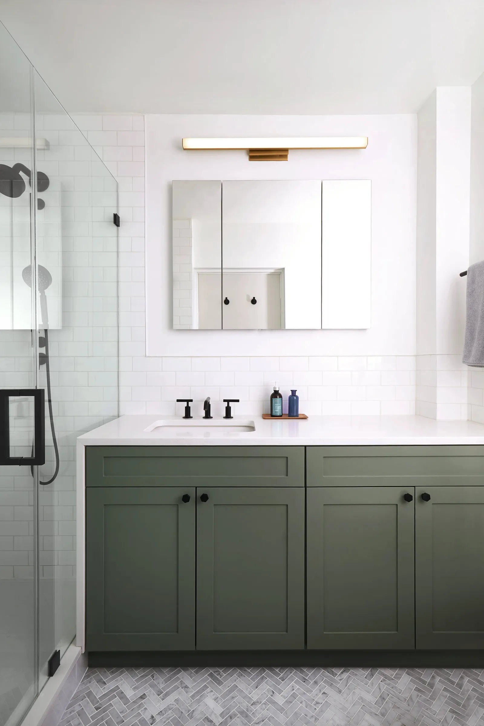 bathroom vanity in sage green with black fixtures, a medicine cabinet mirror and herringbone floor tile