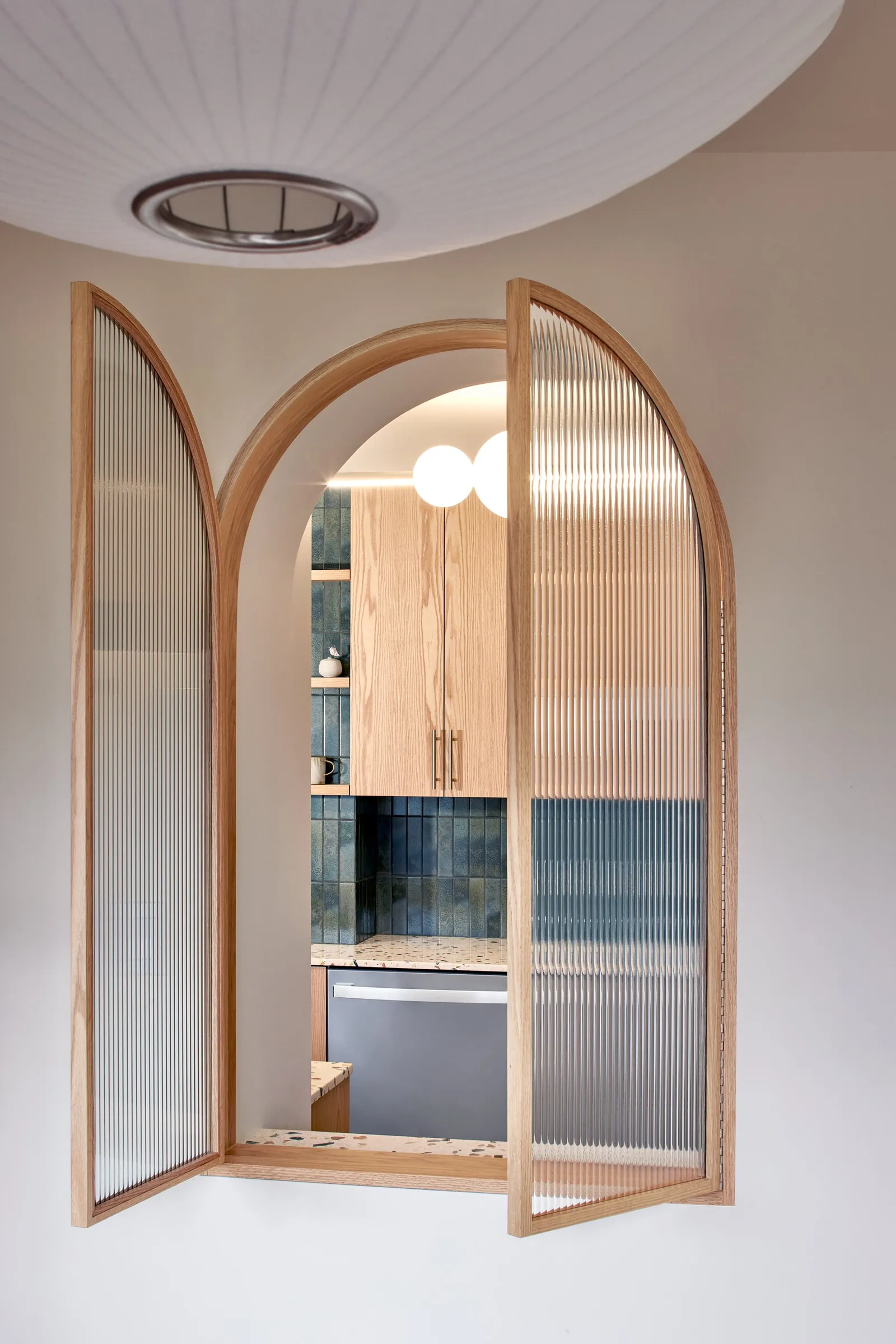 arched fluted-glass window with open panes, looking through to a kitchen with blue tile