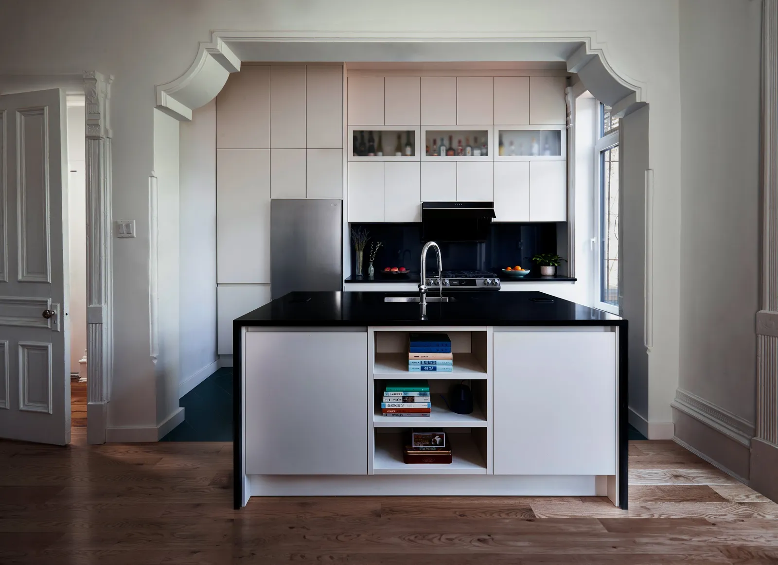 kitchen seen through an arched opening, with a black-topped white island, open shelves and a dark backsplash