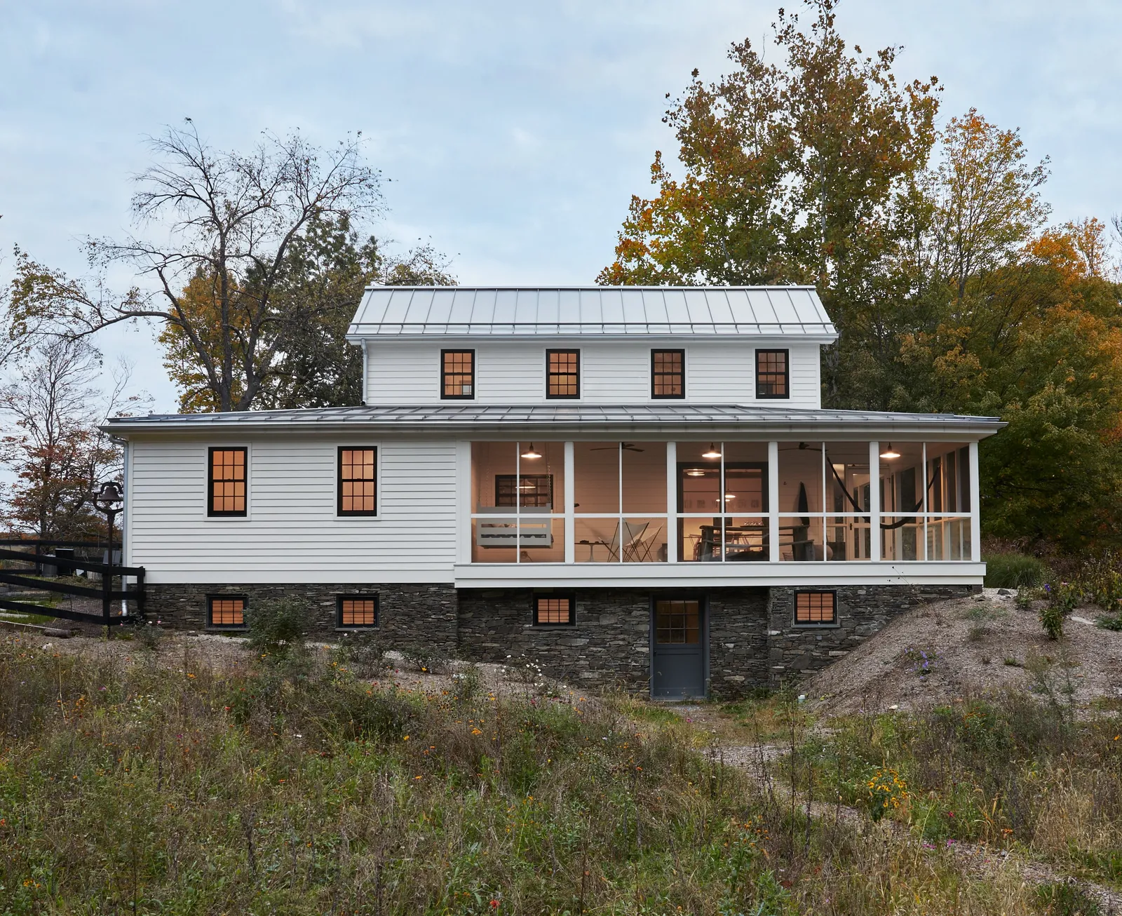 farmhouse side elevation with a stone base, a screened porch and a gray lower door under overcast sky