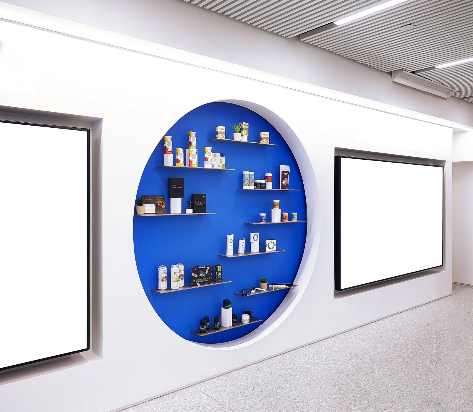round blue niche in a white wall holding small shelves of products, flanked by two blank screens