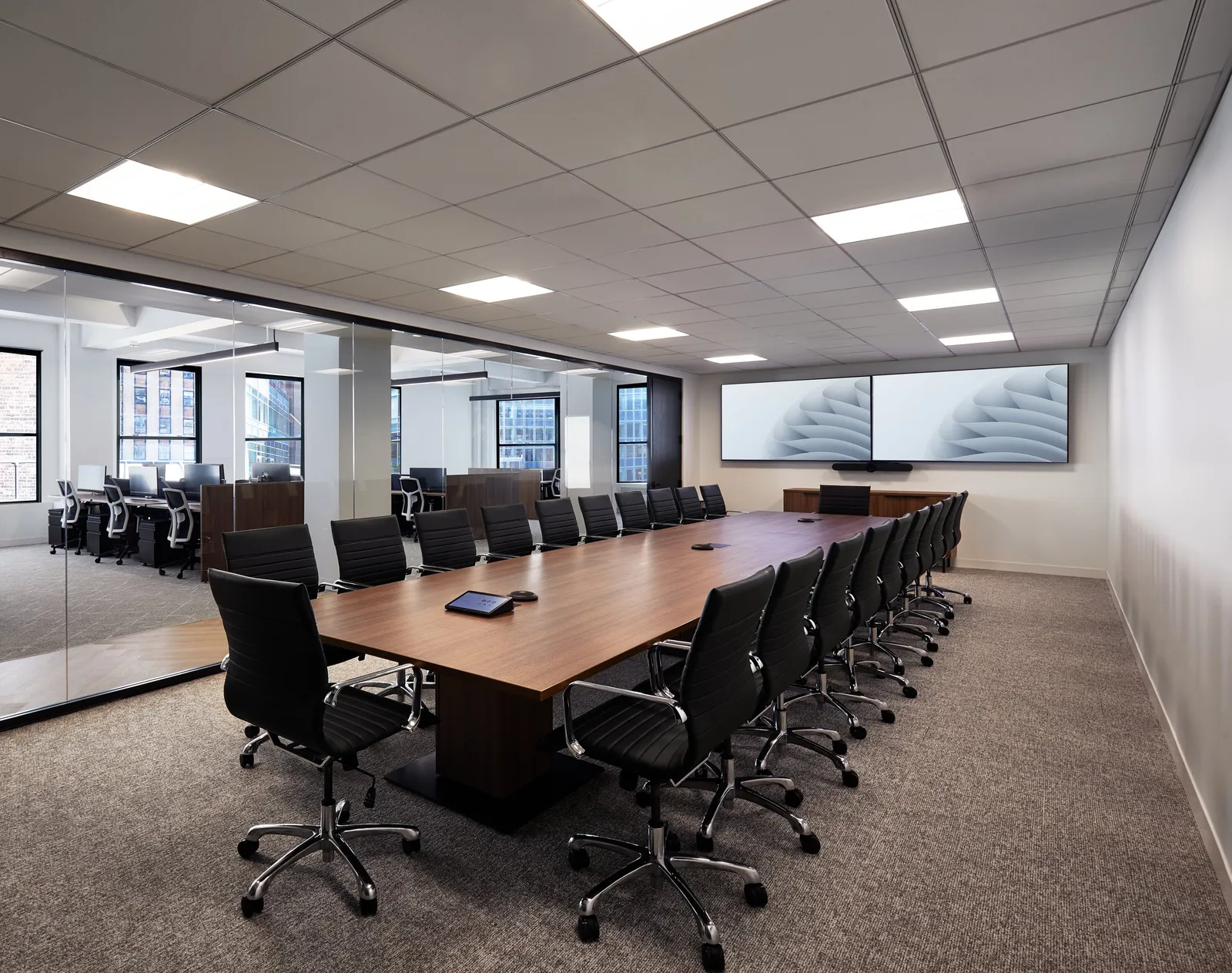 long walnut conference table with black leather chairs, two wall screens and glass wall to open office