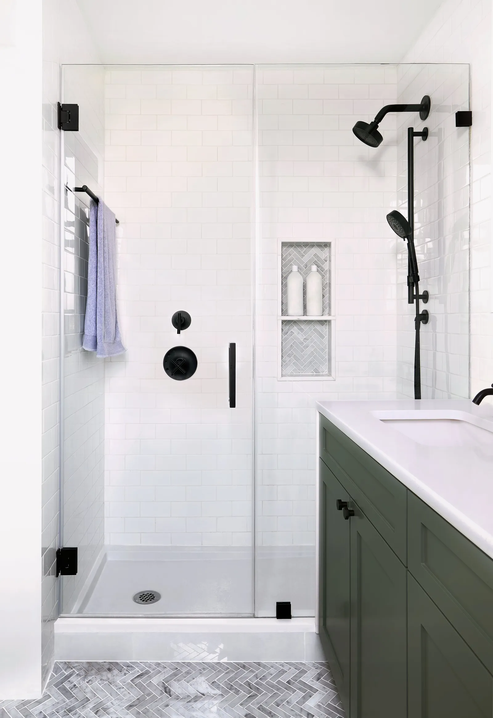 glass-enclosed white tile shower with black fixtures and a niche, beside the green vanity