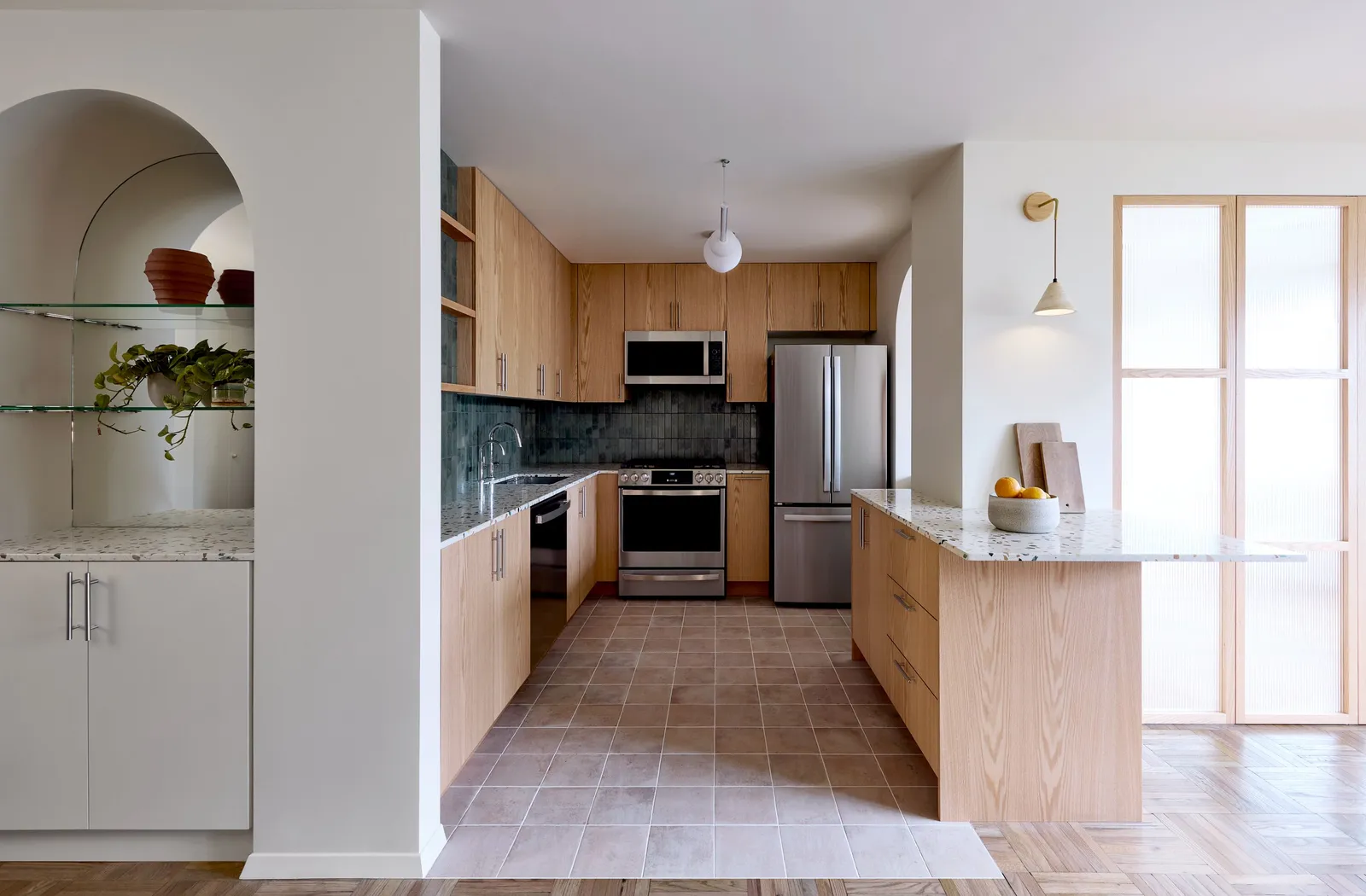kitchen with wood cabinets, an arched shelf niche and a terrazzo-topped peninsula beside glass doors