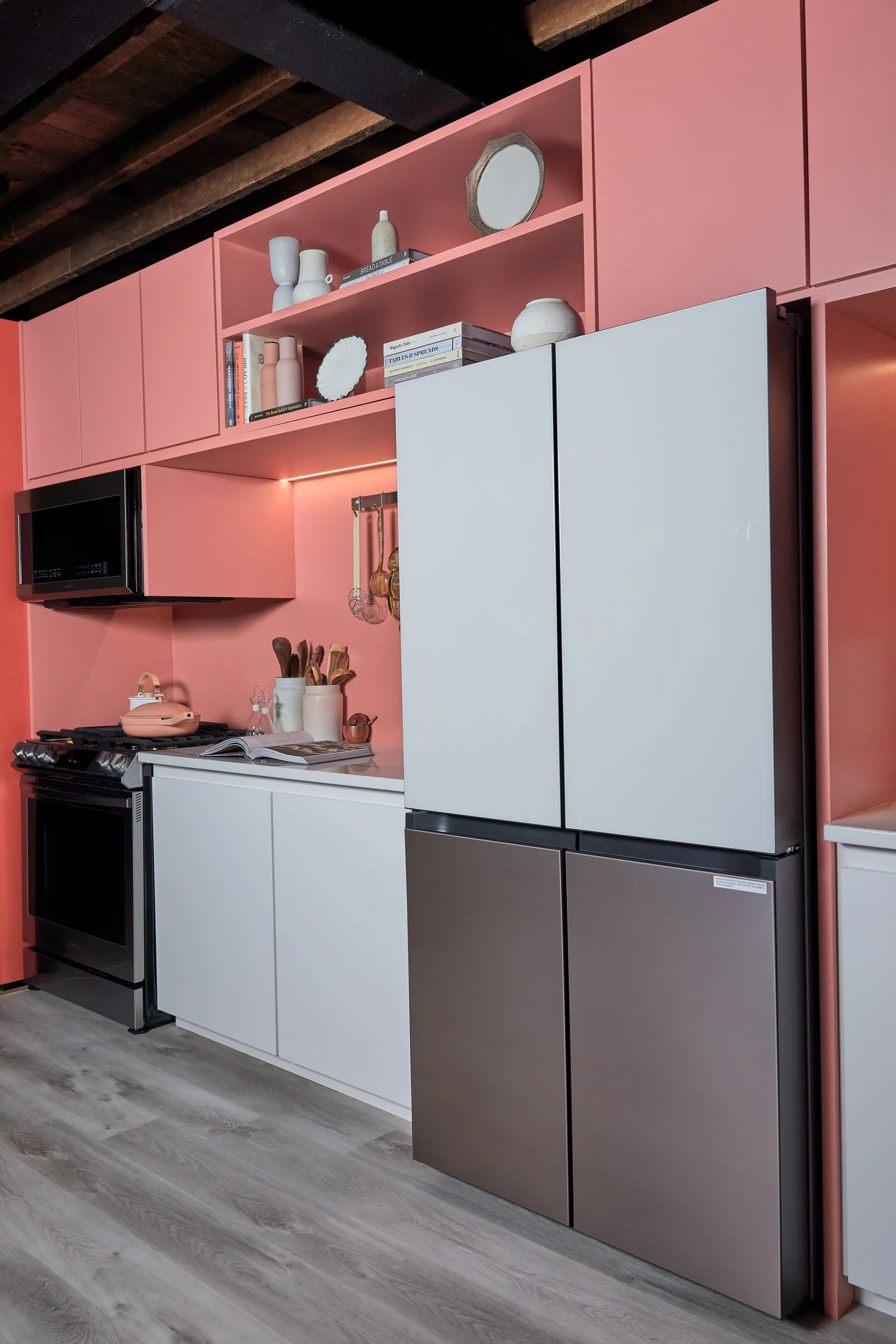 tall view of pink kitchen: four-door refrigerator, range, microwave, open shelf and wood-beam ceiling
