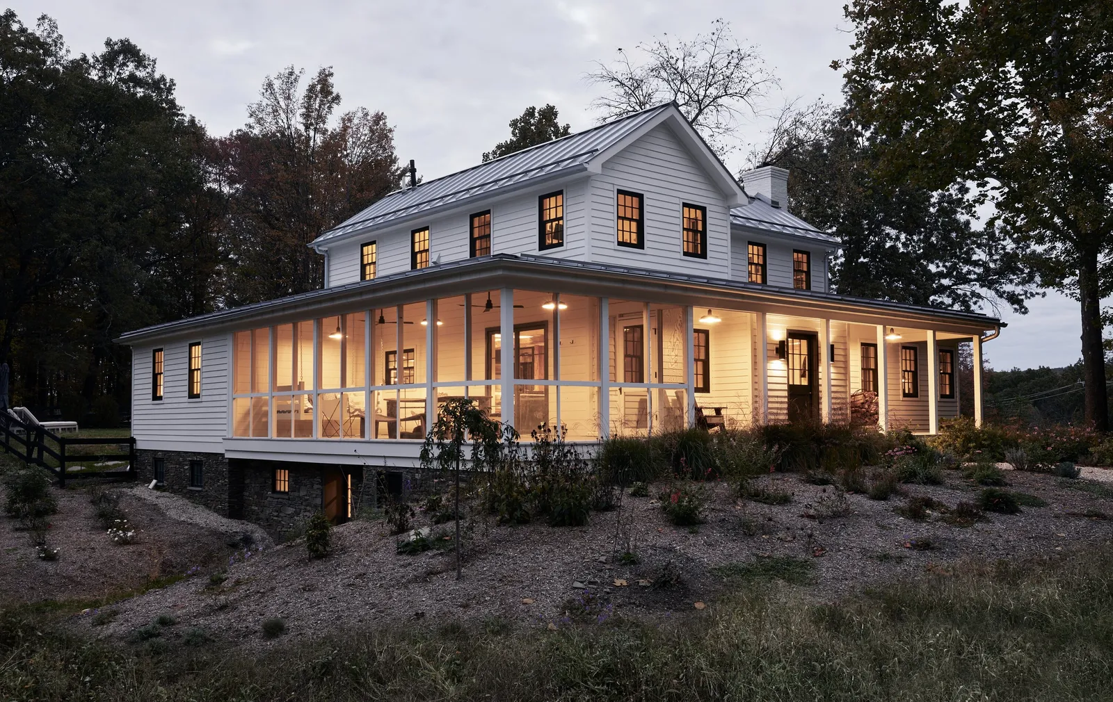 farmhouse at dusk, the screened porch glowing with warm light against dark trees