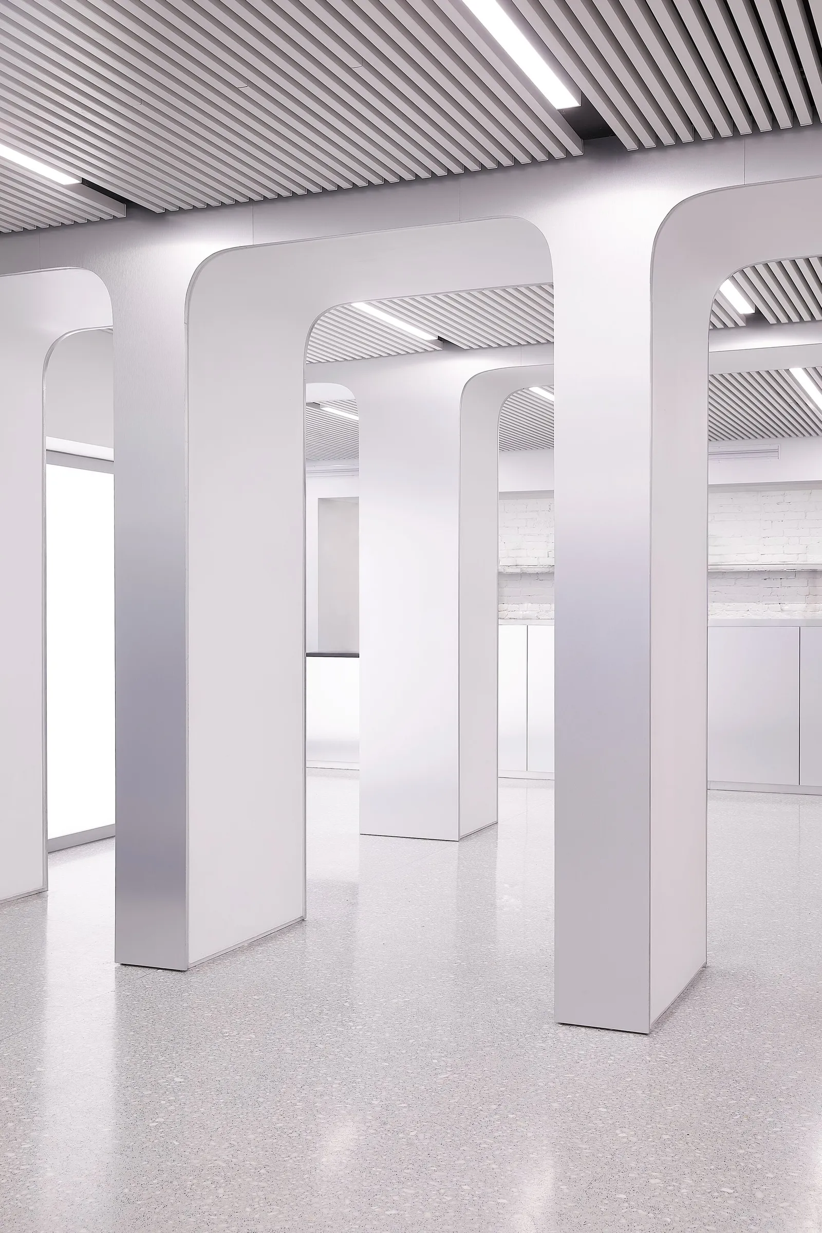 white rounded columns with brushed metal edges rising to a slatted ceiling above a pale speckled floor
