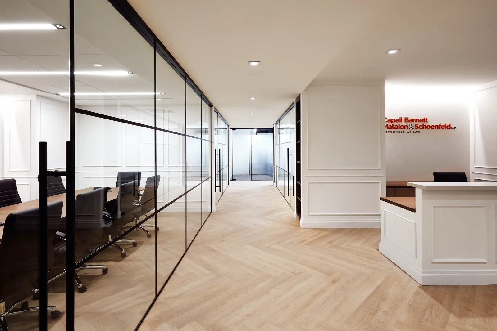 herringbone hallway with a glass-walled conference room on the left and reception desk at the end
