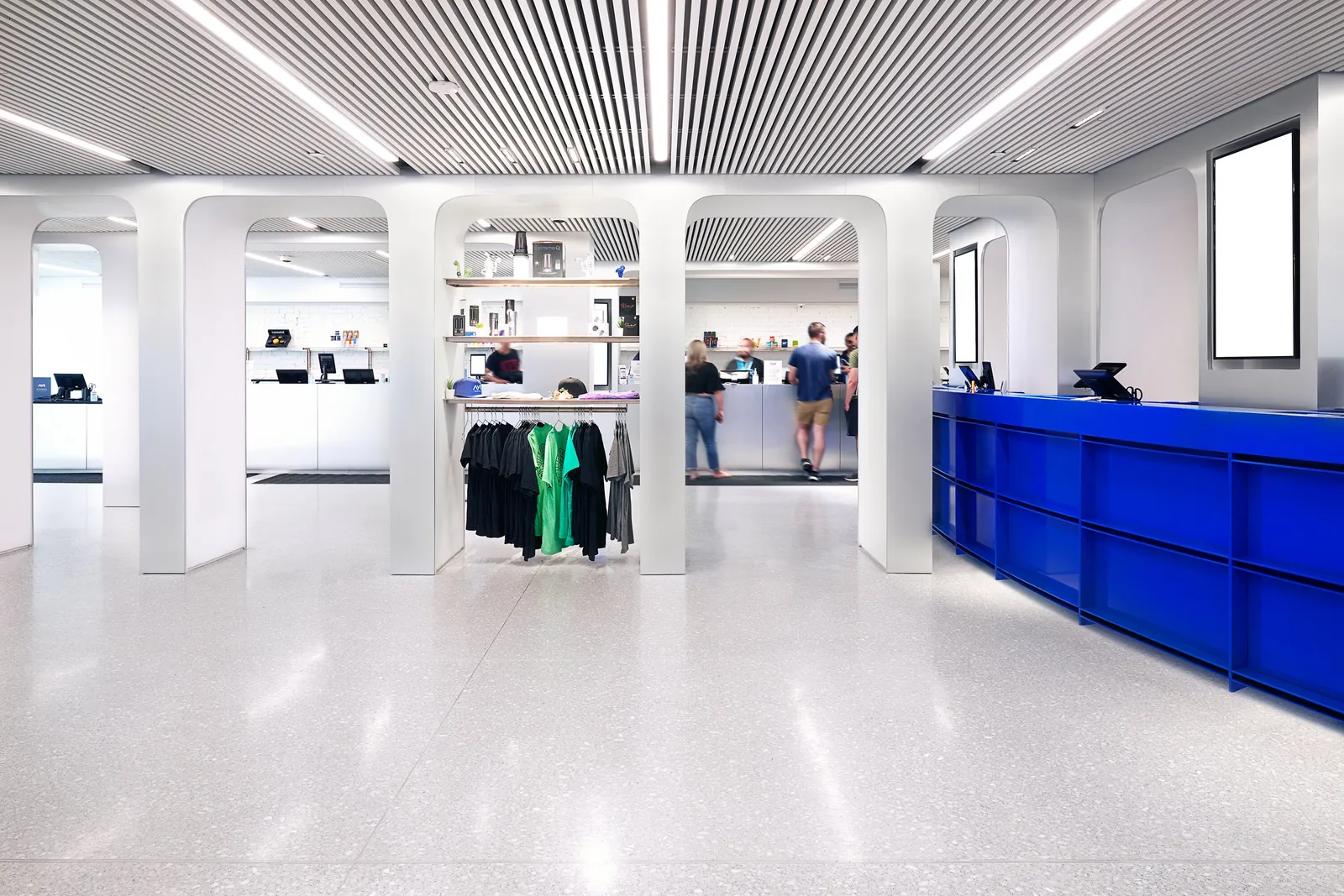 wide view down the shop: arched white columns, a clothing rack, customers, and the blue counter on the right
