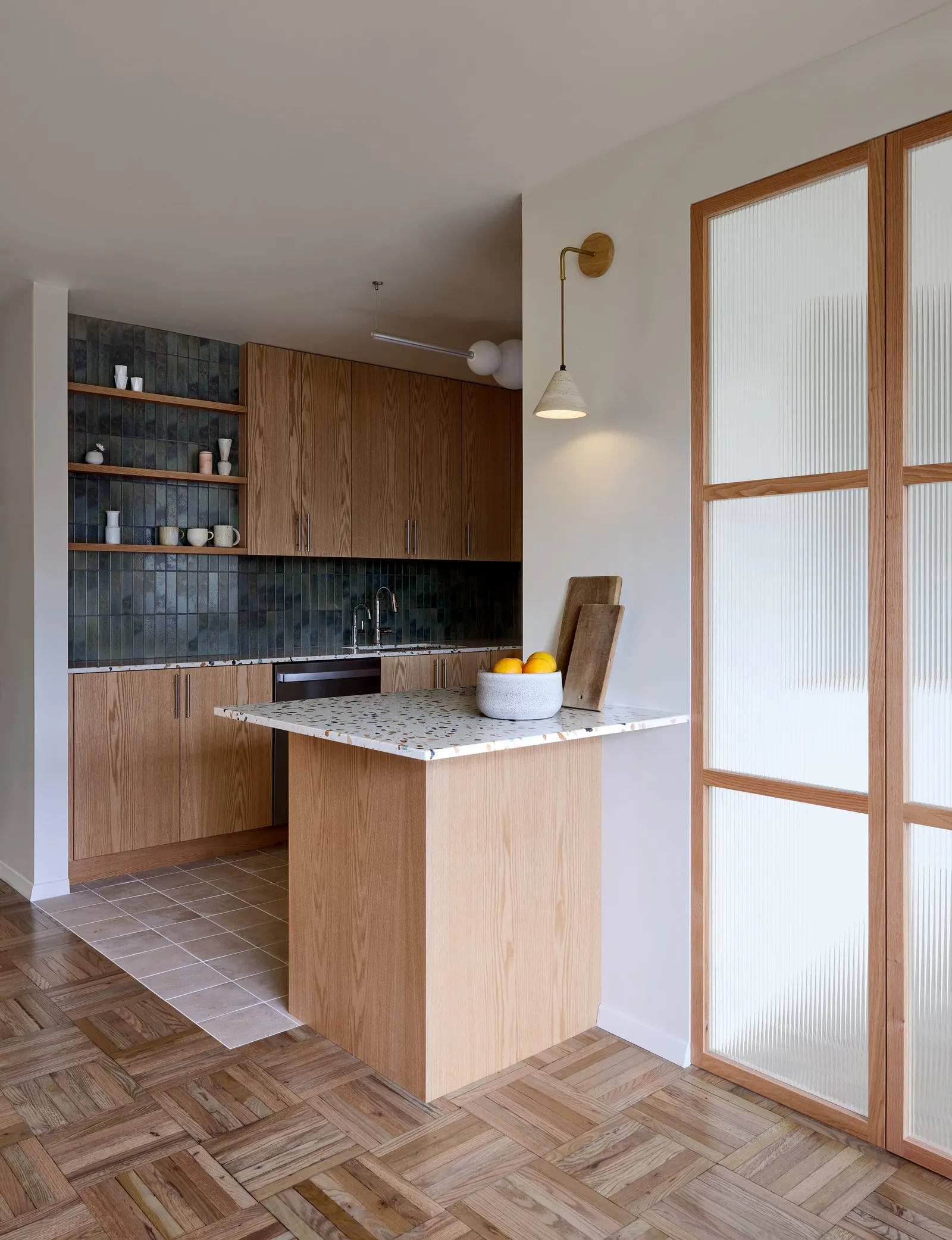 kitchen peninsula with a bowl of oranges next to a fluted-glass and wood door, on a parquet floor