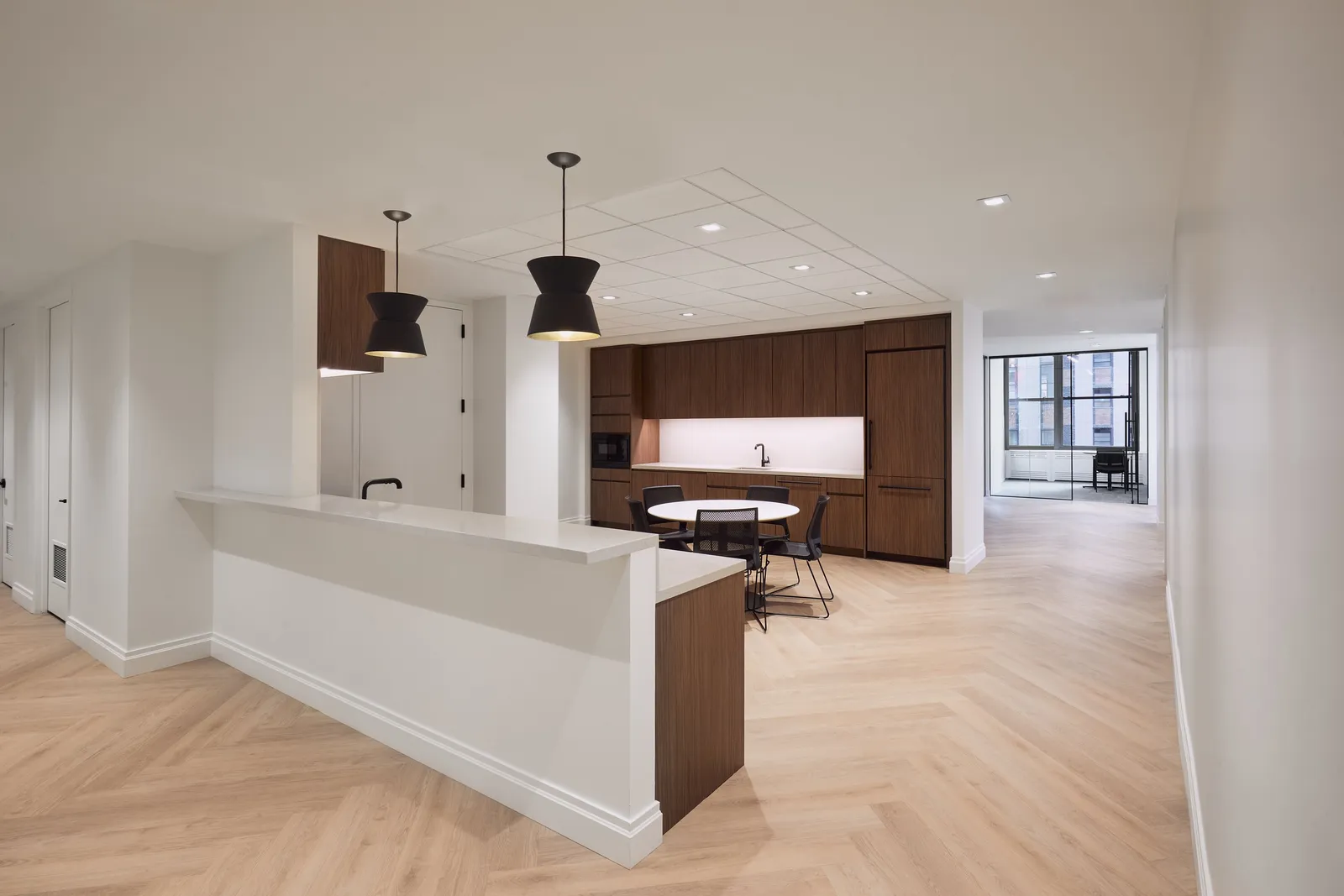 open kitchen with walnut cabinets, white counter, two black pendant lamps and a small round table