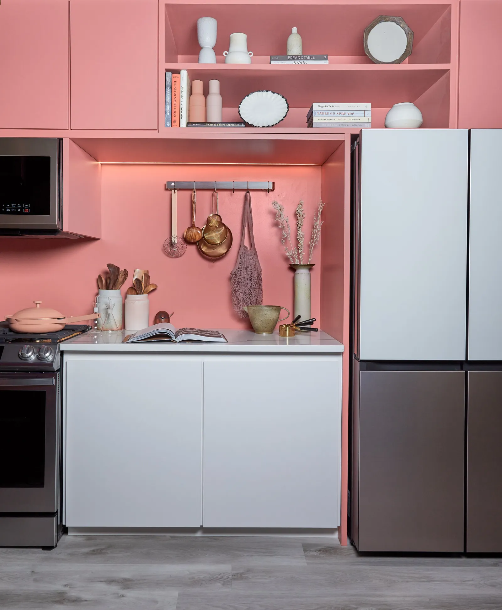 closer view of pink kitchen with hanging copper utensils, open cookbook, range and white lower cabinets
