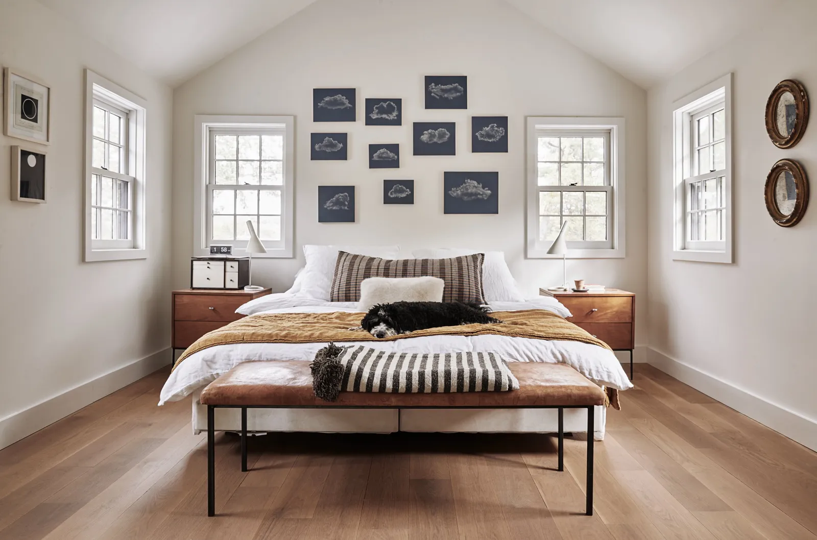 bedroom with a peaked ceiling, a bed with a leather bench and a grid of blue prints above the headboard
