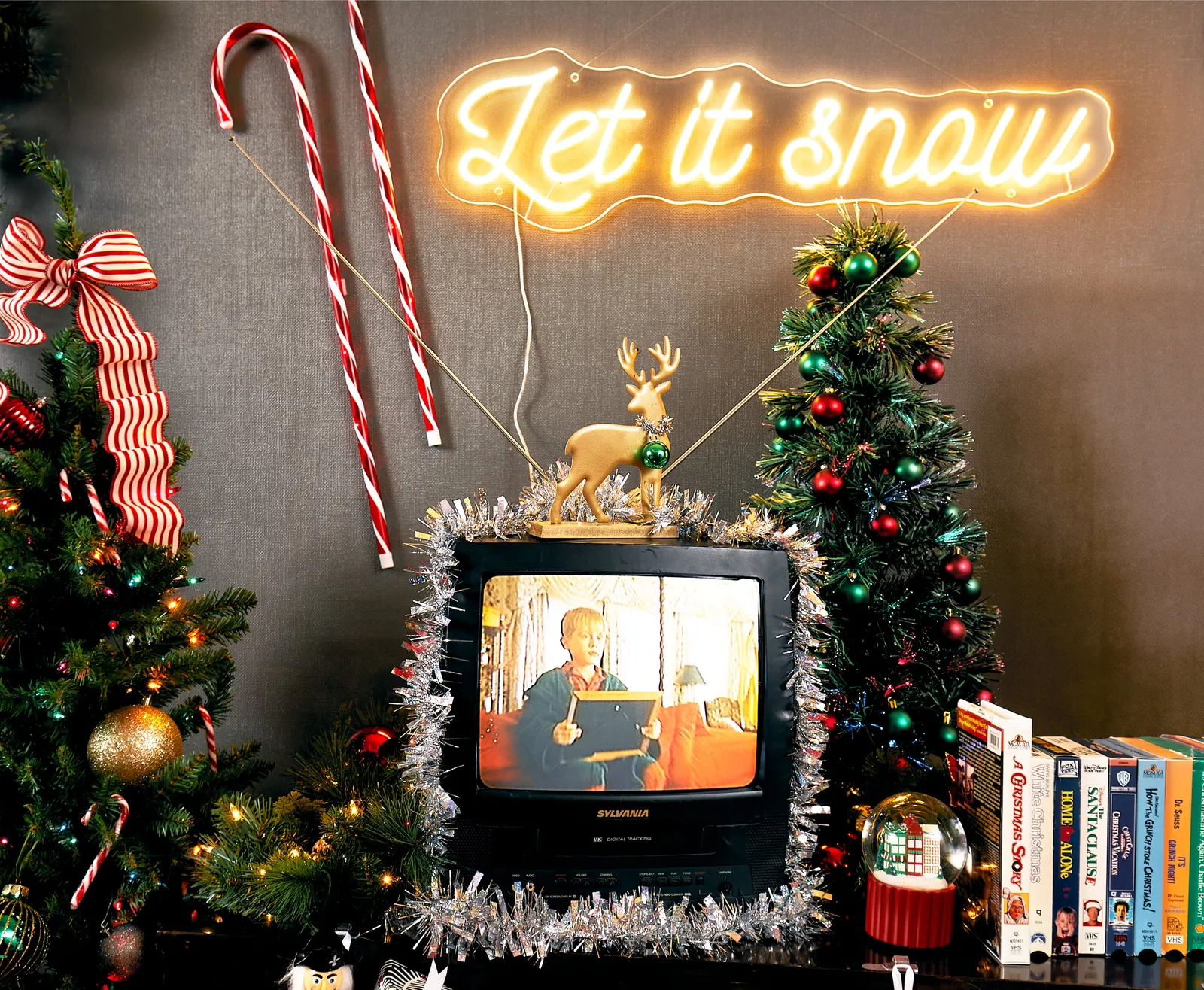 retro tv wrapped in tinsel under a glowing "let it snow" neon sign, with candy canes and a small tree