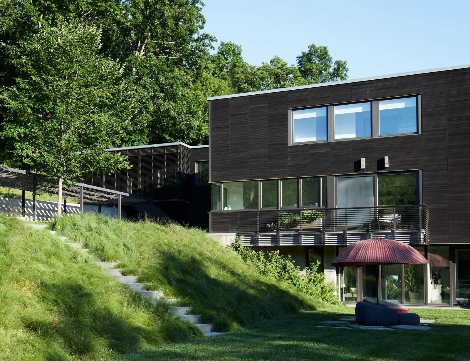 house exterior with charred-wood cladding, grassy slope with stone steps and a red umbrella on the lawn
