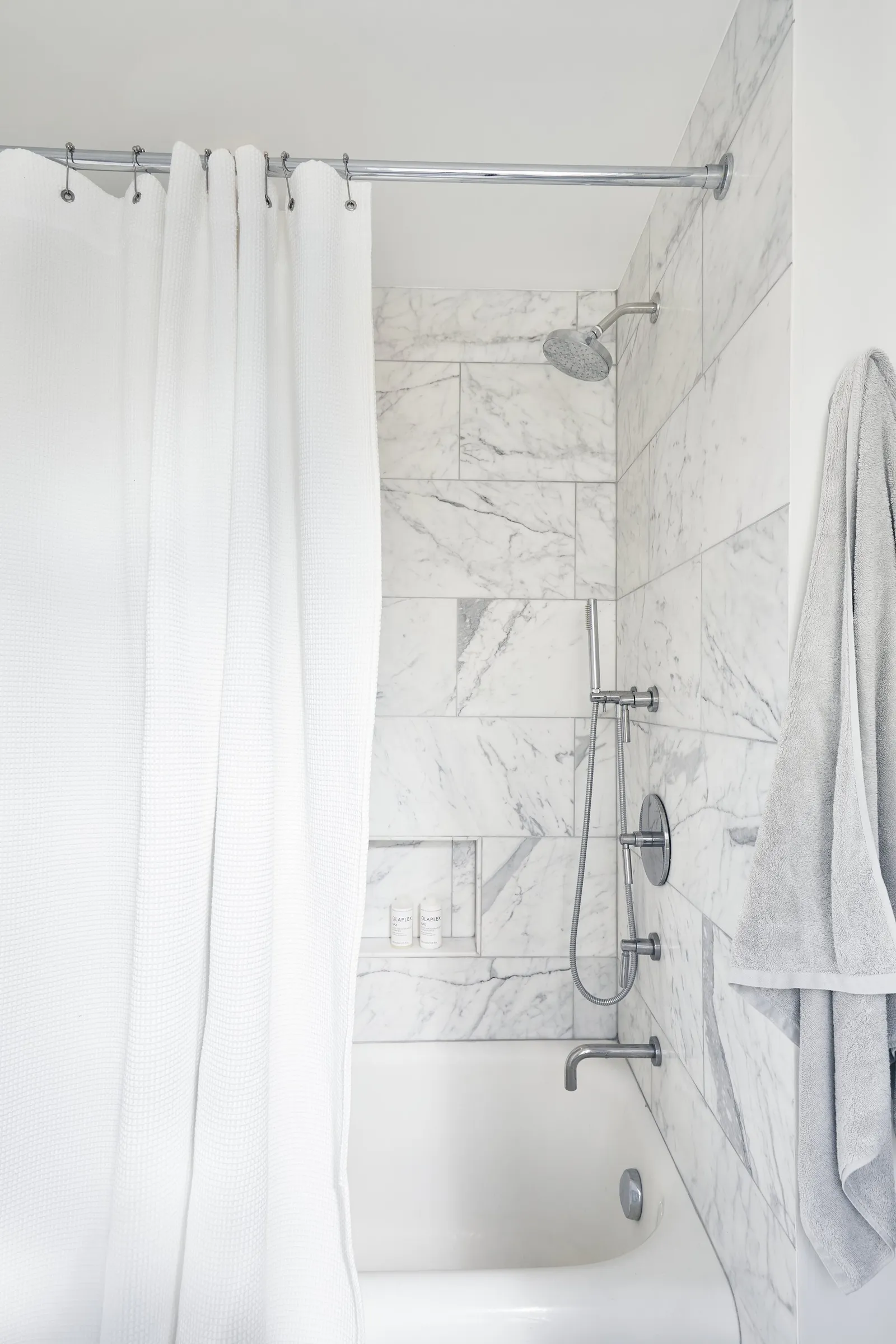 marble-tiled tub and shower with a white curtain pulled back and a gray towel