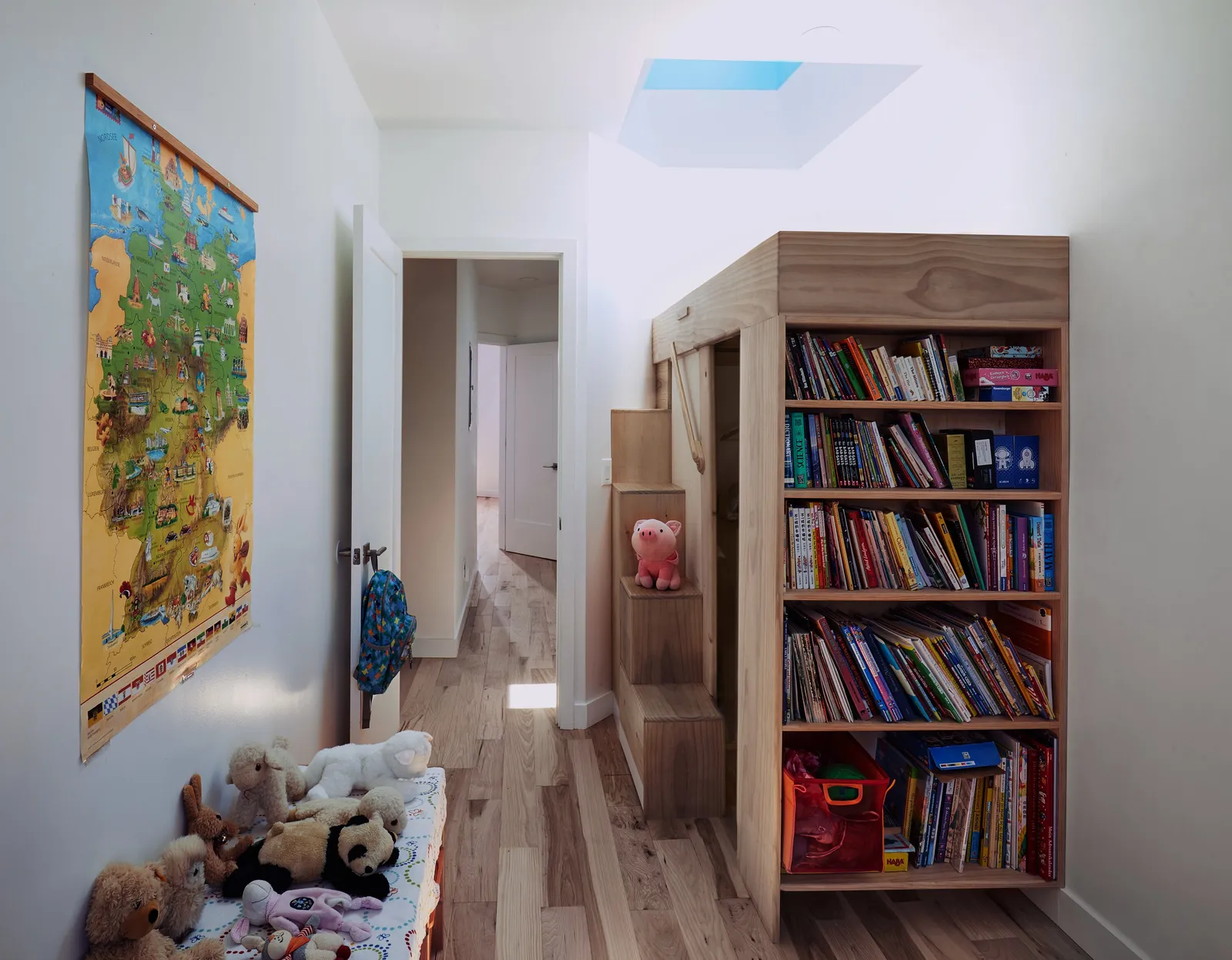 hallway with a world map poster, a bench of stuffed animals and a tall wooden bookcase under a skylight