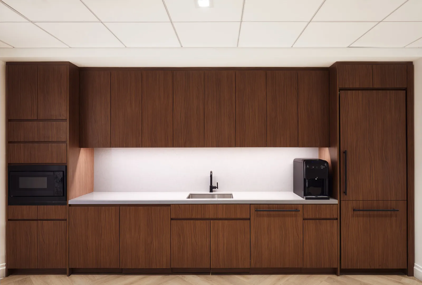 straight-on wall of walnut kitchen cabinets with built-in microwave, sink and a black coffee maker