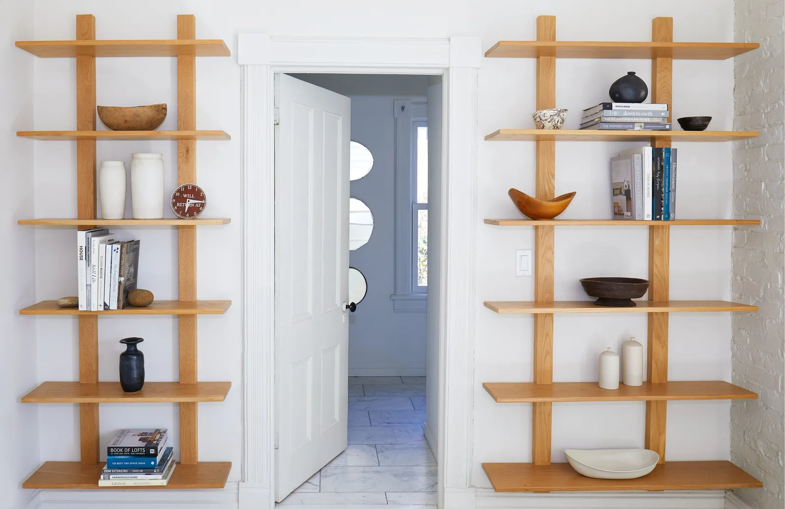 two tall wooden ladder-style shelves holding bowls and books on either side of an open door