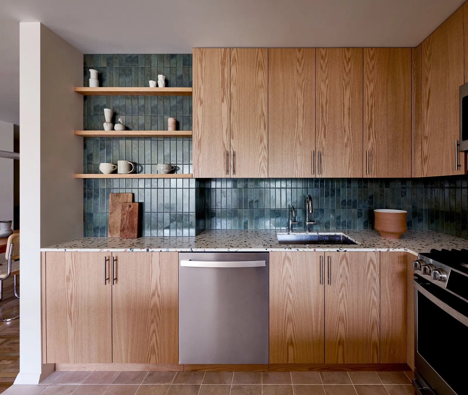 kitchen counter with wood cabinets, stainless dishwasher, blue-green tile backsplash and open shelves