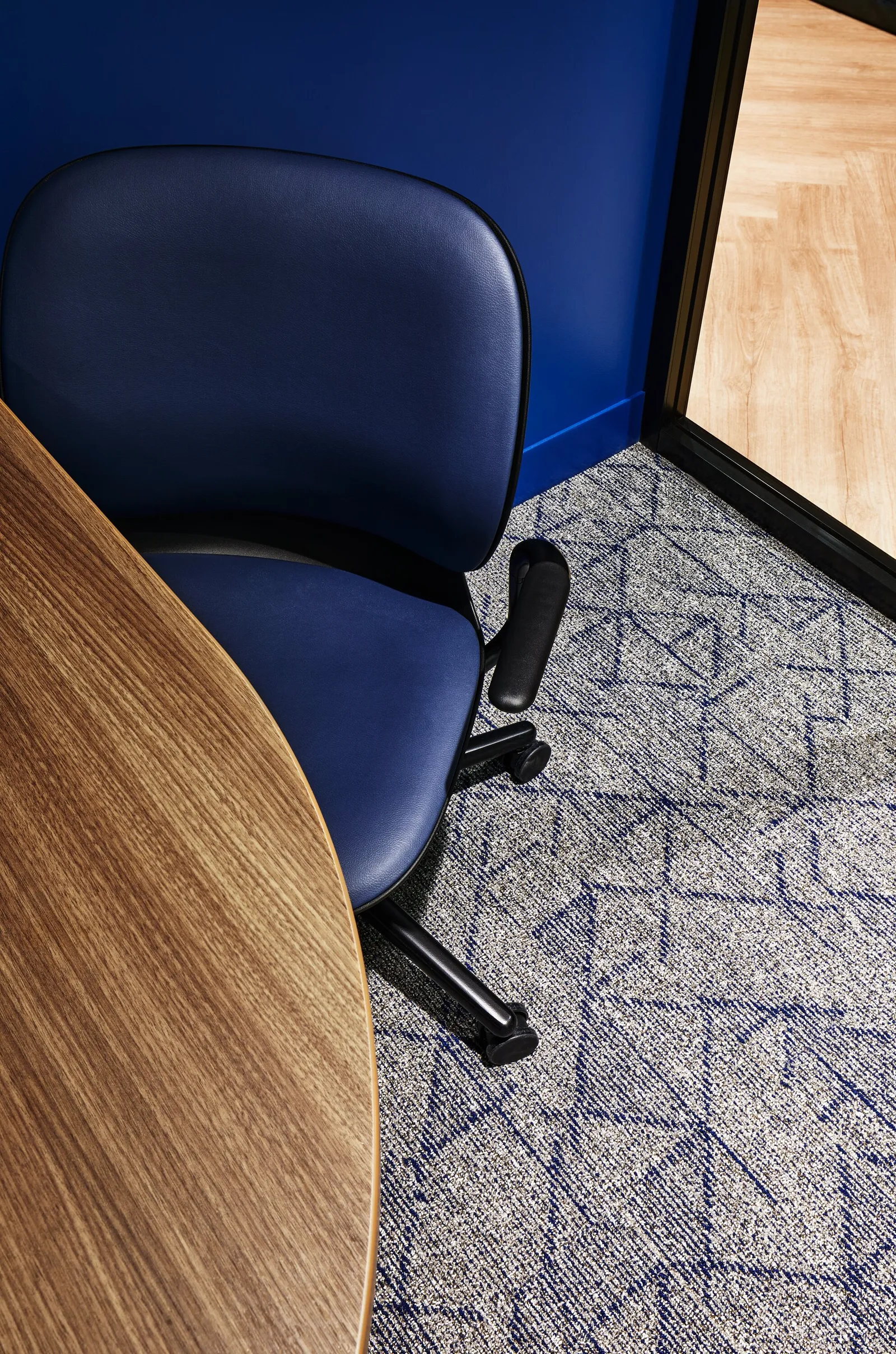 overhead view of a navy chair at a curved wood table, blue wall and geometric blue-gray carpet