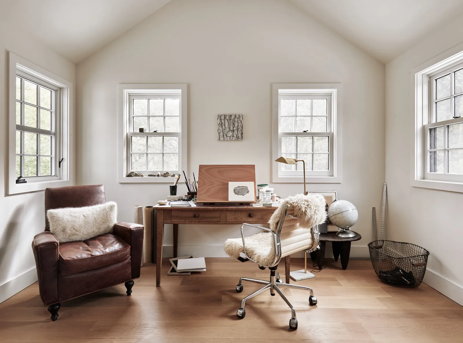 attic office with a wooden desk, a brown leather armchair, a sheepskin-covered chair and a globe