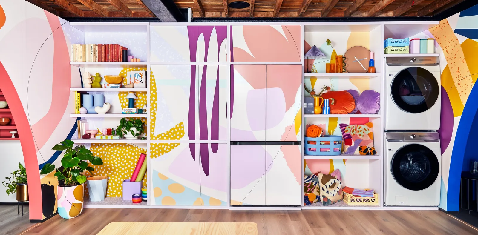 colorful mural wall with matching refrigerator doors, shelves of books and baskets, and stacked washer and dryer