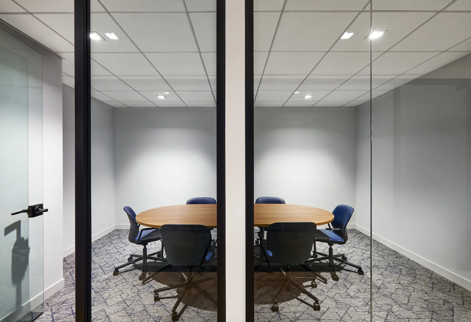 small round-table meeting room seen through two glass panels, blue chairs and patterned carpet