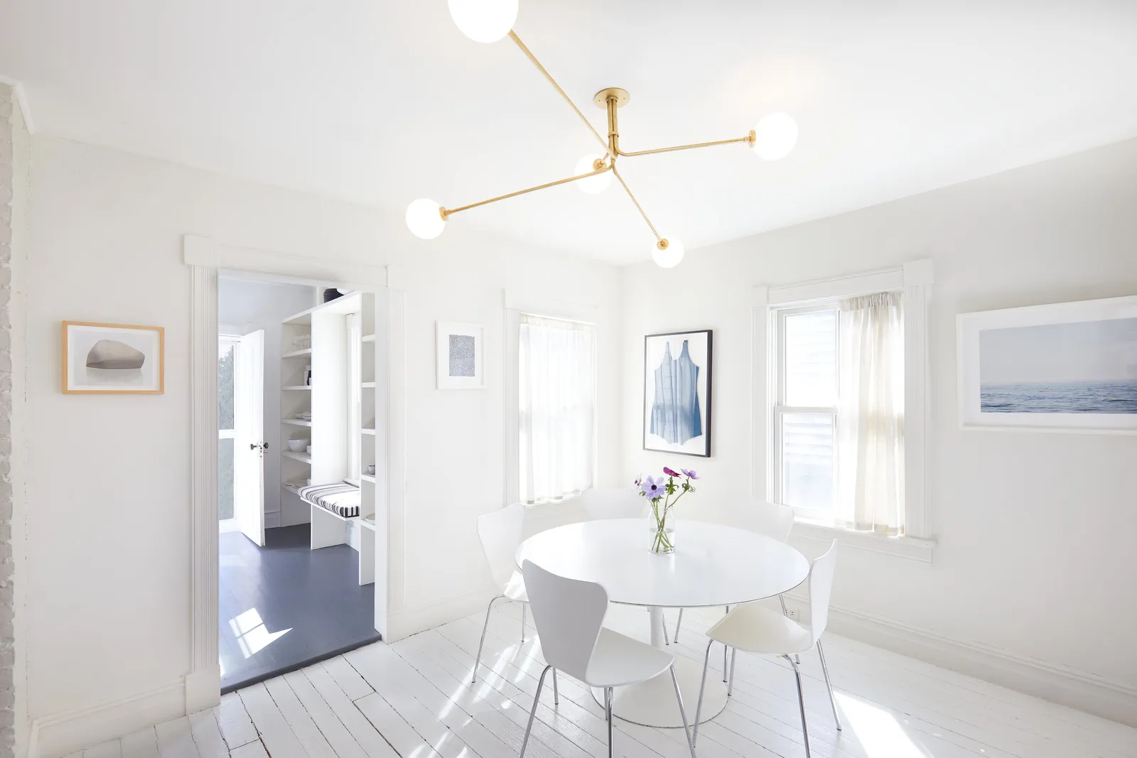 dining room with a round white table, white chairs, framed art and a brass ceiling fixture with globe lights