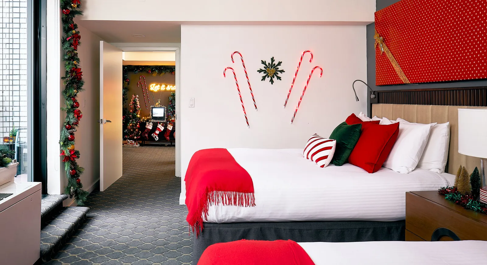 bedroom with white bedding, red throw and pillows, candy cane wall lights and a giant red wrapped gift above the bed