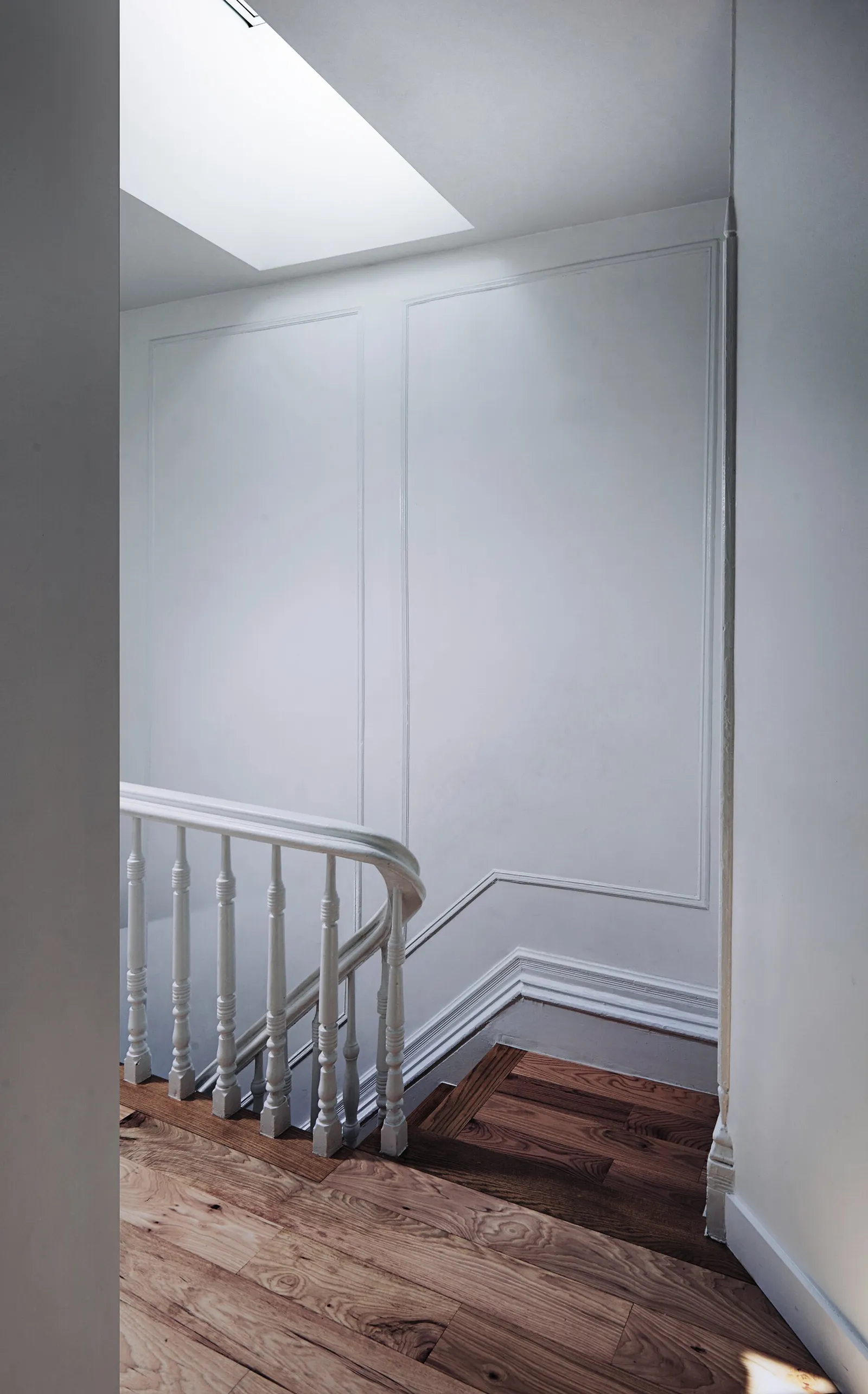 white paneled stairwell landing with turned white balusters, a skylight and warm wood floor
