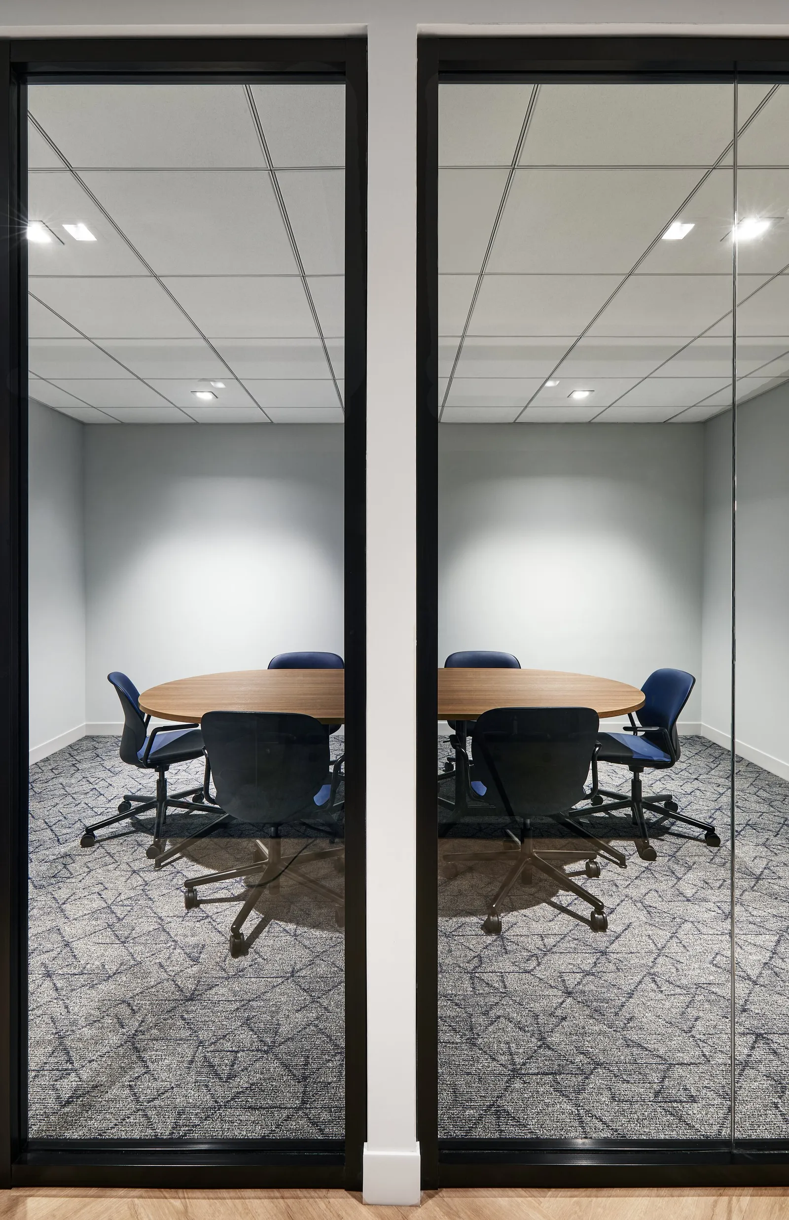narrow framing of a round-table room through black-framed glass, blue chairs, soft ceiling lights