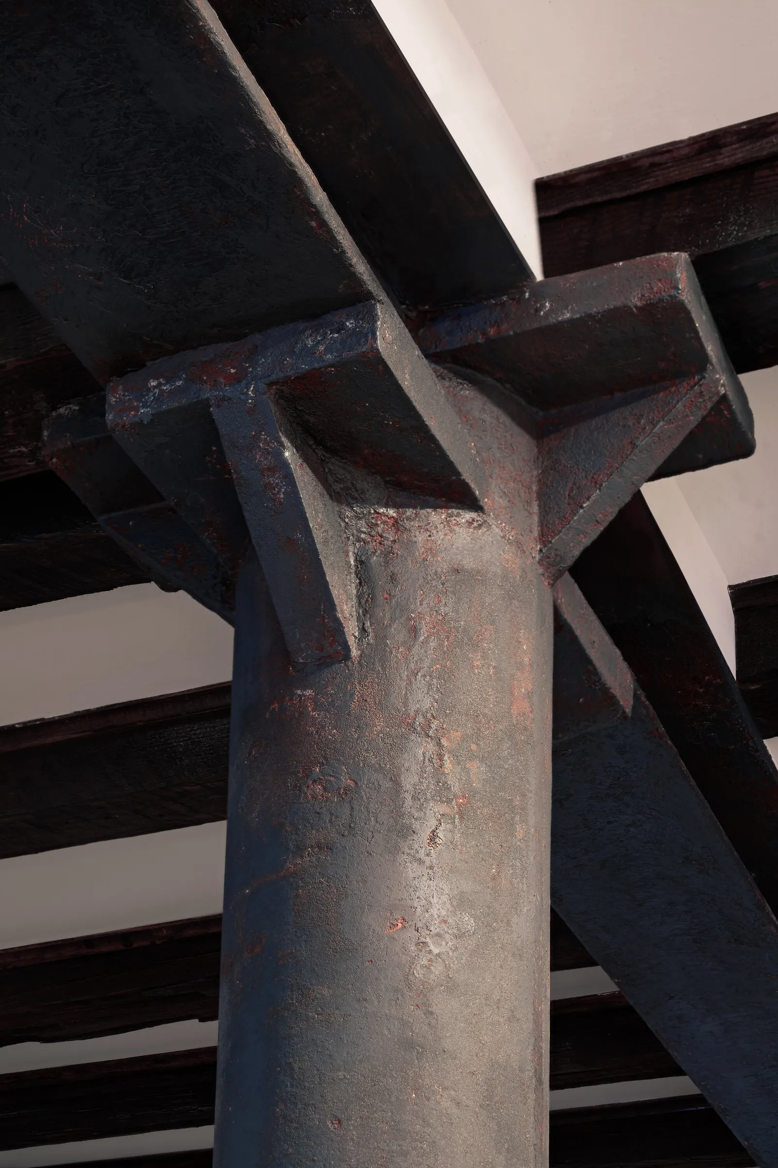 close detail of a rusted dark iron column and bracket meeting heavy wood ceiling beams