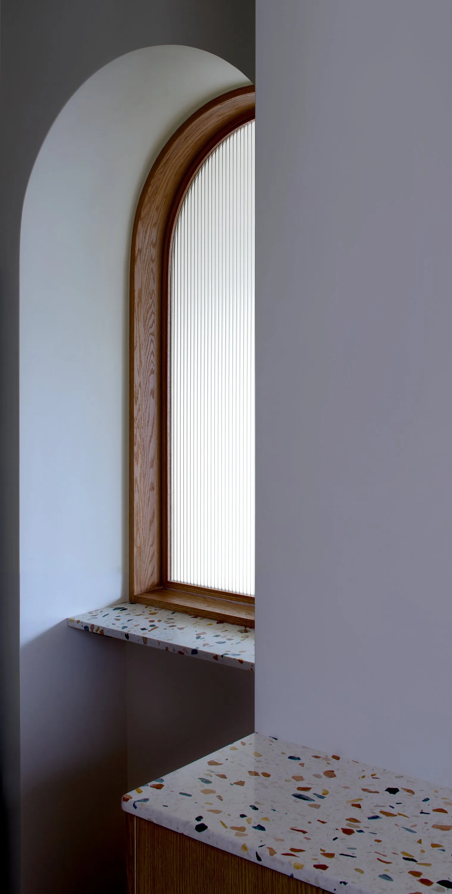 arched window with fluted glass above a terrazzo sill in a shadowed corner