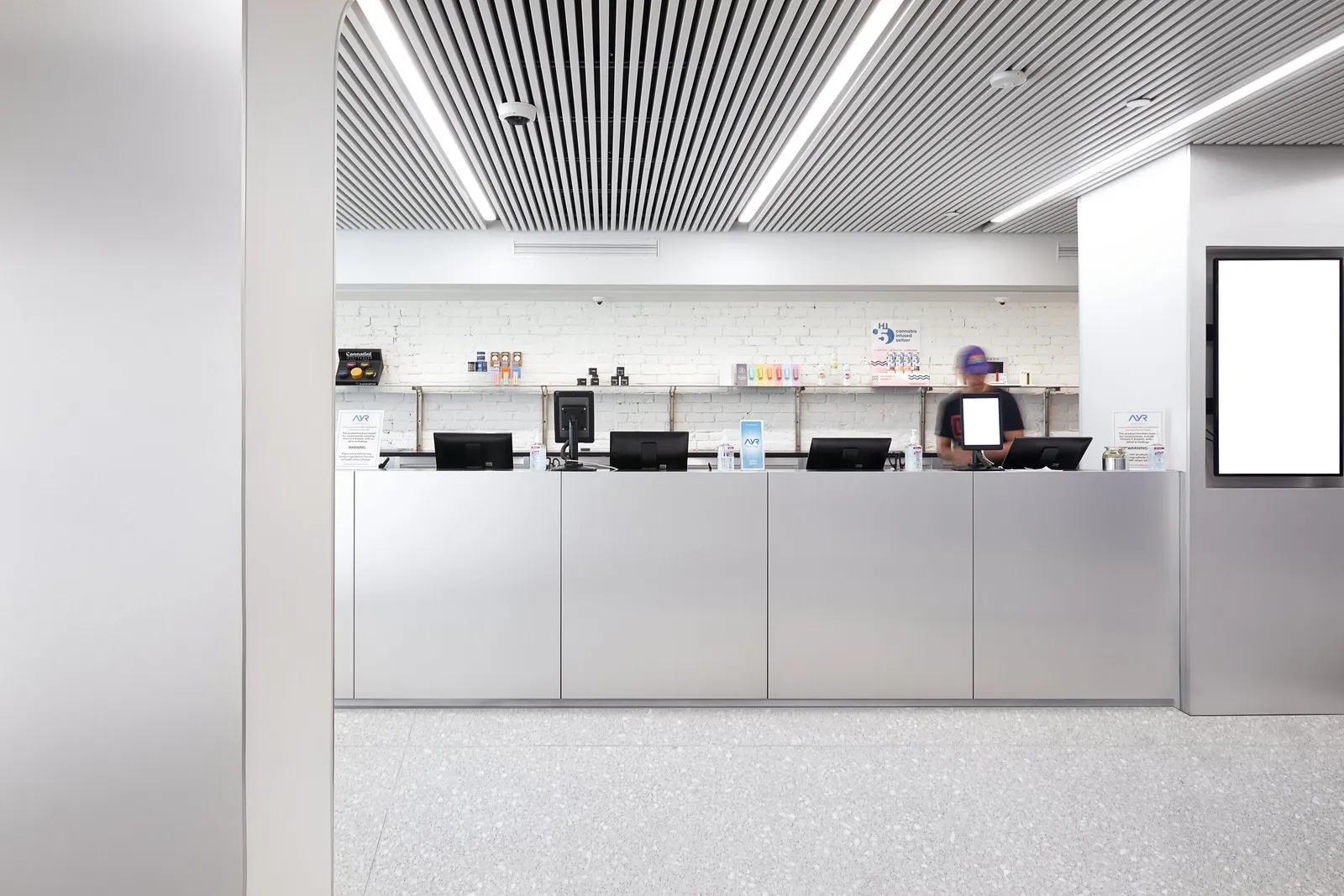 customers' side of a silver paneled counter with registers, a blank sign, and a white brick wall behind