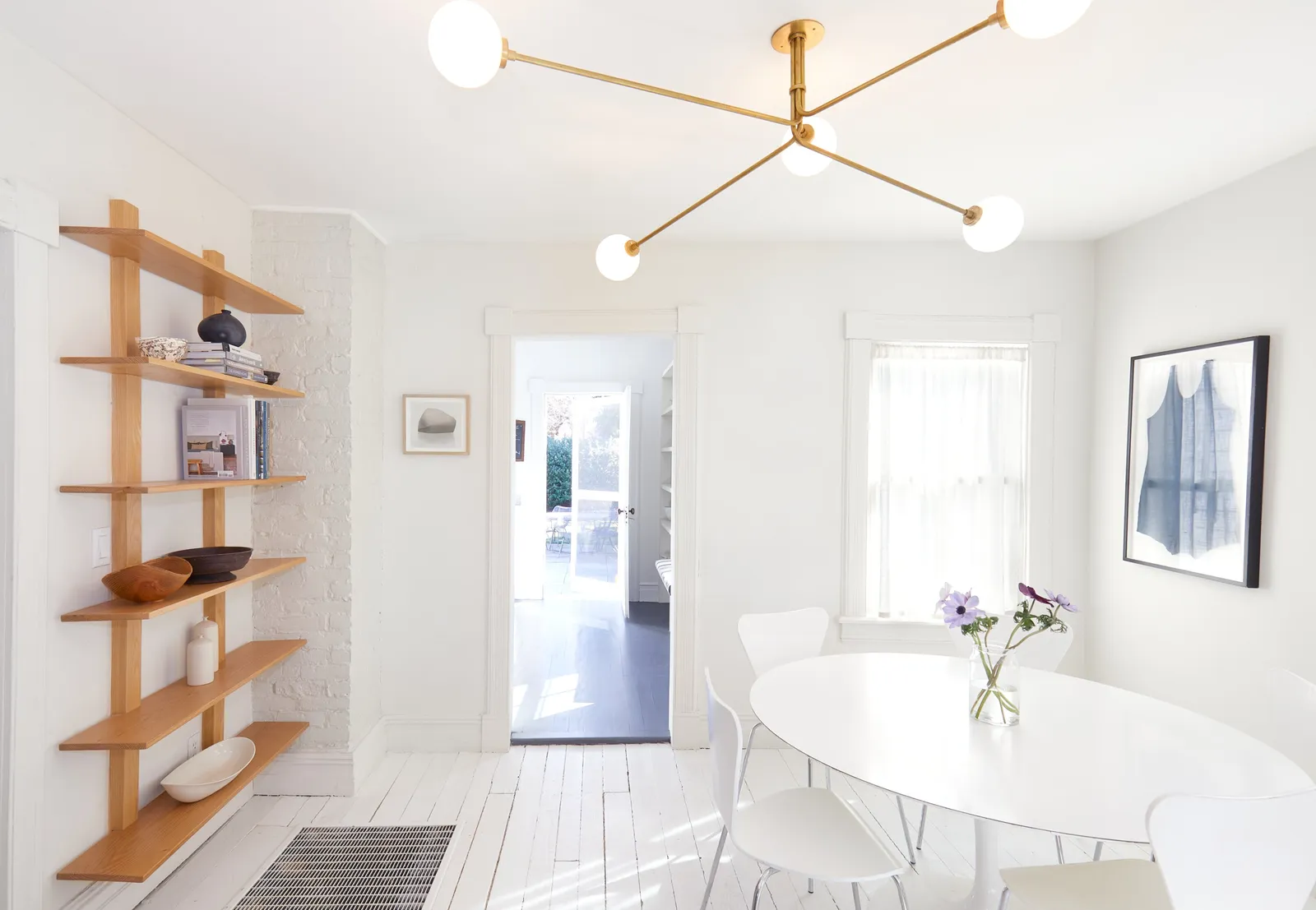 dining room seen from another angle, with the wooden shelves, an oval white table and a brass globe chandelier