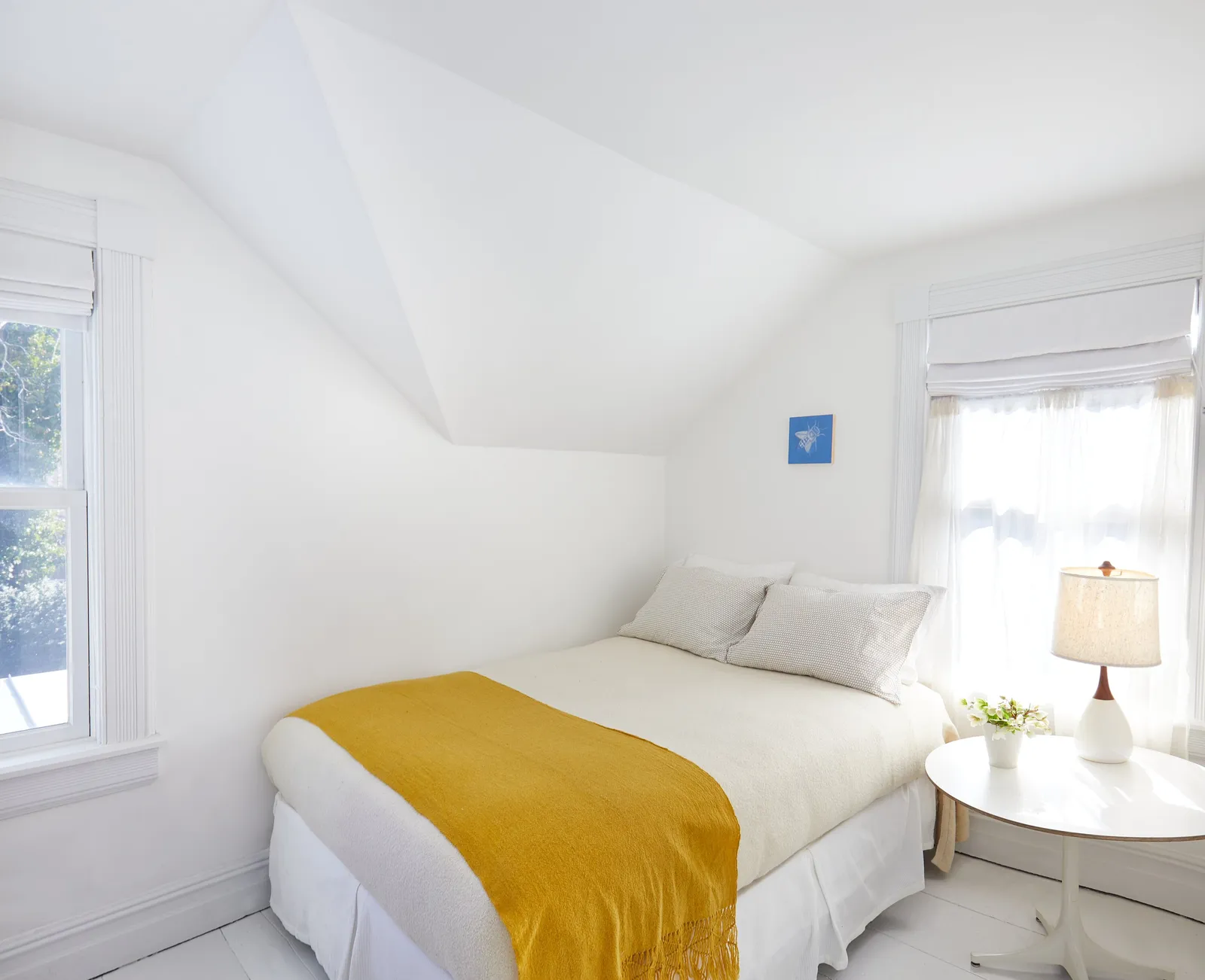 bedroom under a sloped ceiling with a mustard-yellow throw on the bed and a round white side table