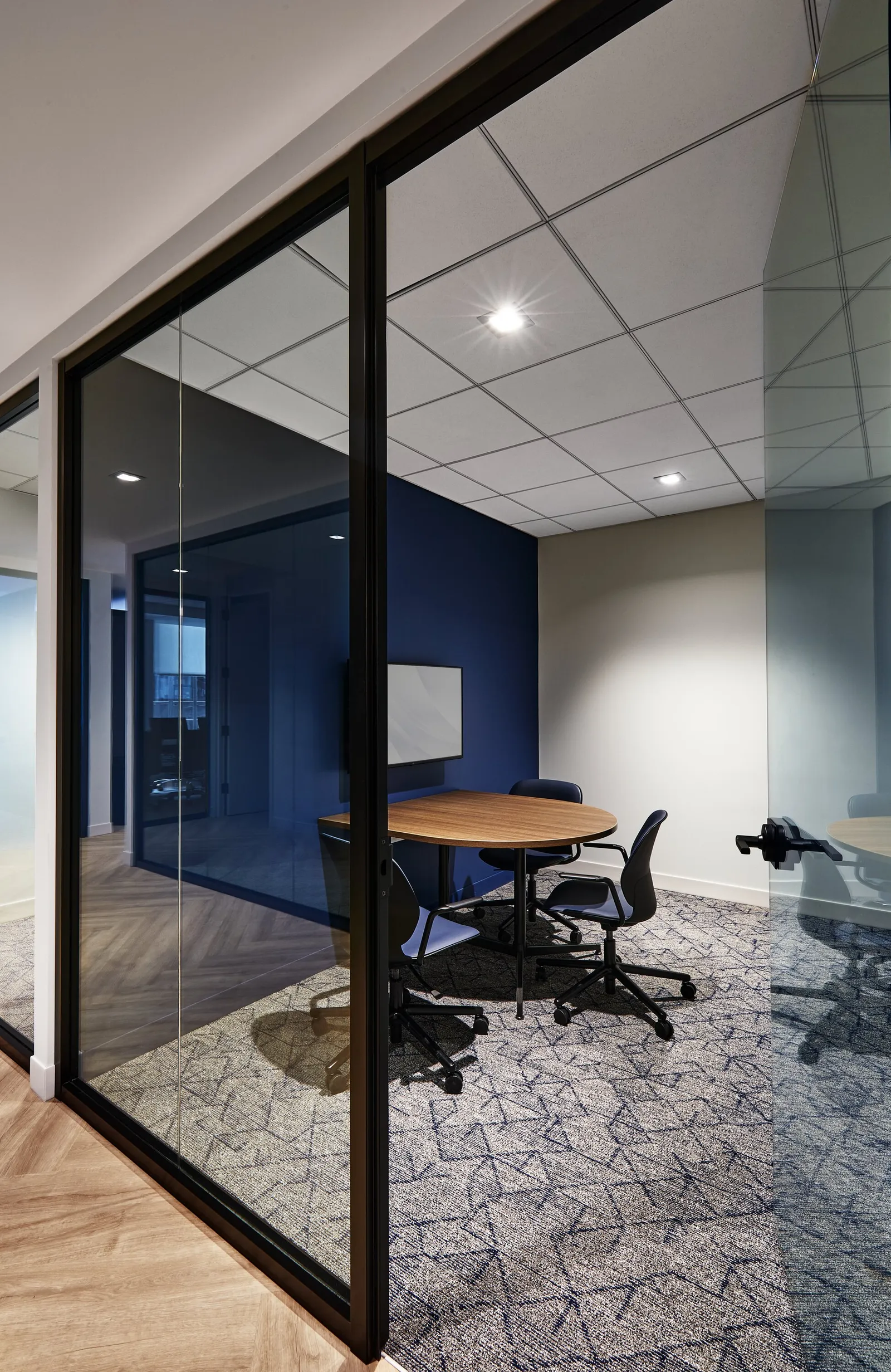 corner meeting room with deep blue wall and round table seen through angled glass partition