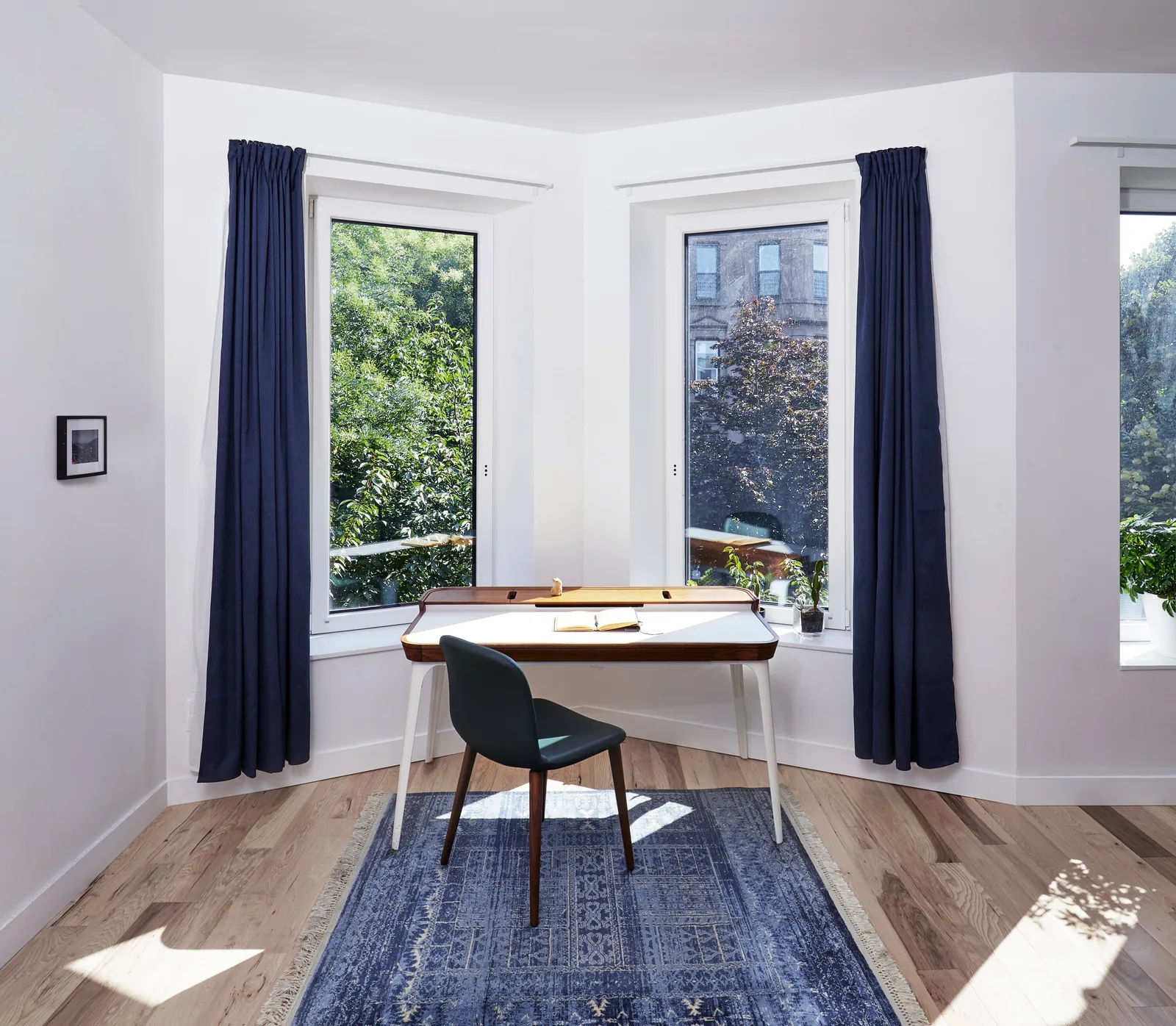 corner room with a small desk and green chair on a blue patterned rug between two windows with navy curtains