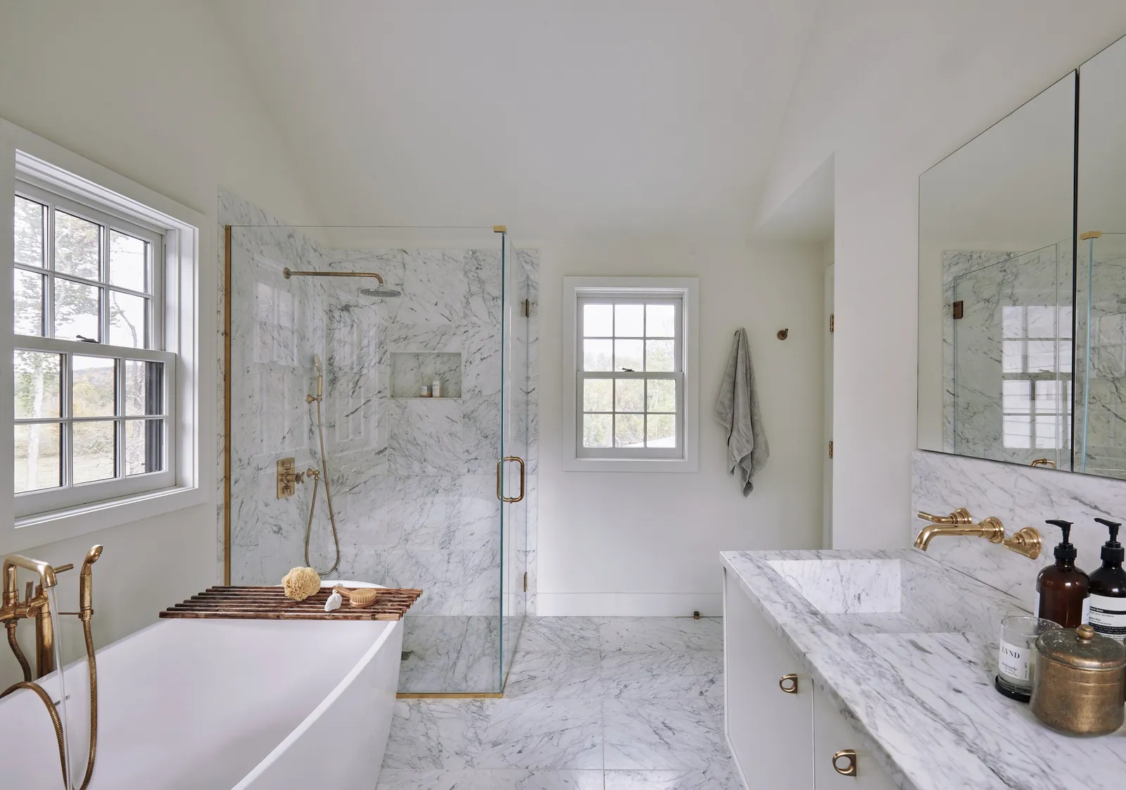 bathroom with a marble-clad shower, a long marble vanity with brass taps and a large mirror