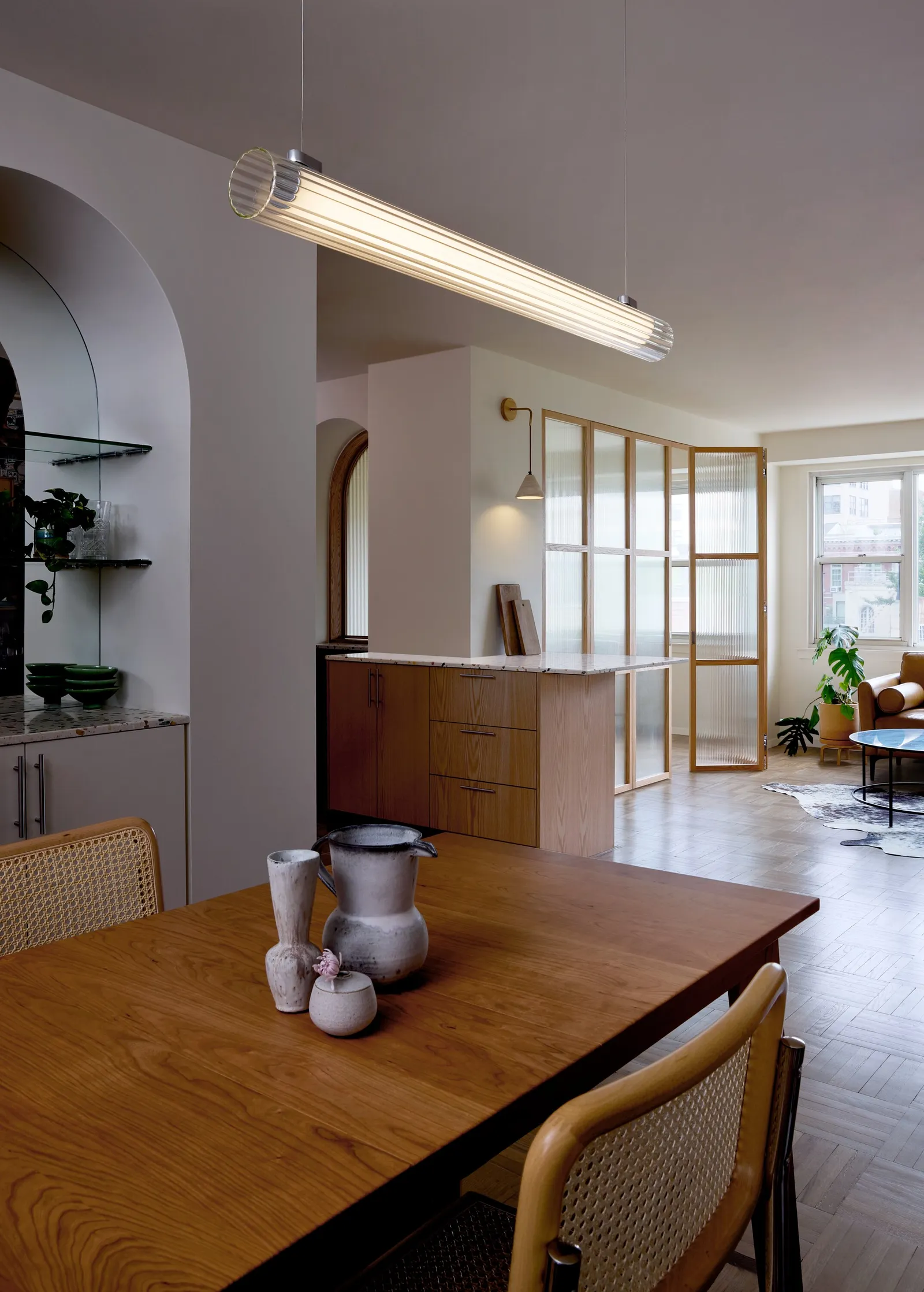 dining table with caned chairs and a ceramic pitcher, a long light fixture and the kitchen beyond